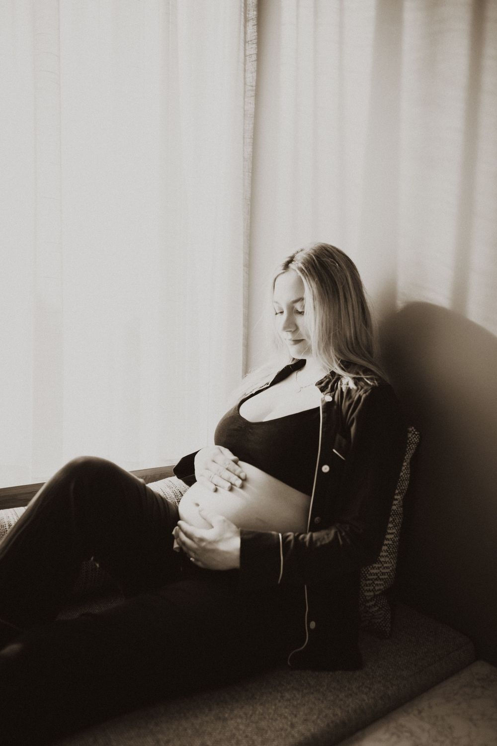 Indoor maternity session with moody black and white photography against white curtains.