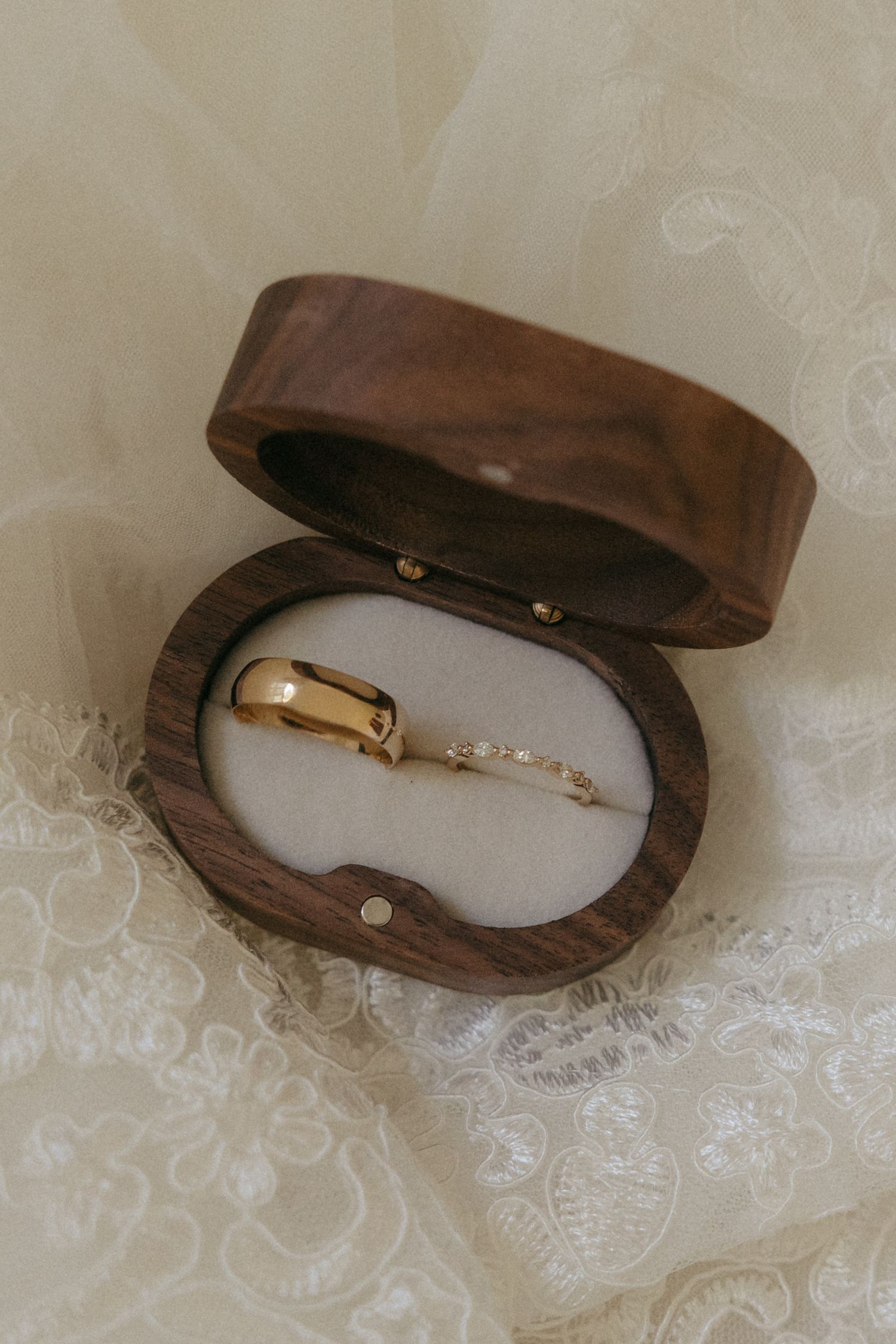 Gold wedding bands displayed in an open wooden ring box on delicate white lace fabric.