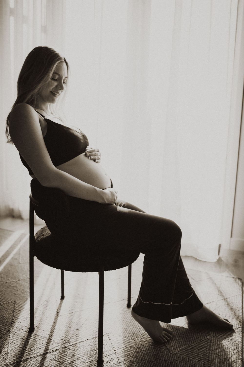 Silhouette of pregnant woman sitting in chair by window in dramatic lighting.