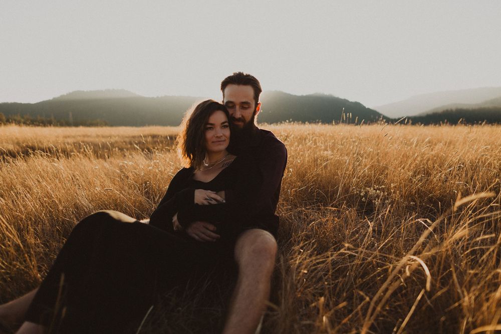 A couple sitting together in a golden wheat field at sunset.