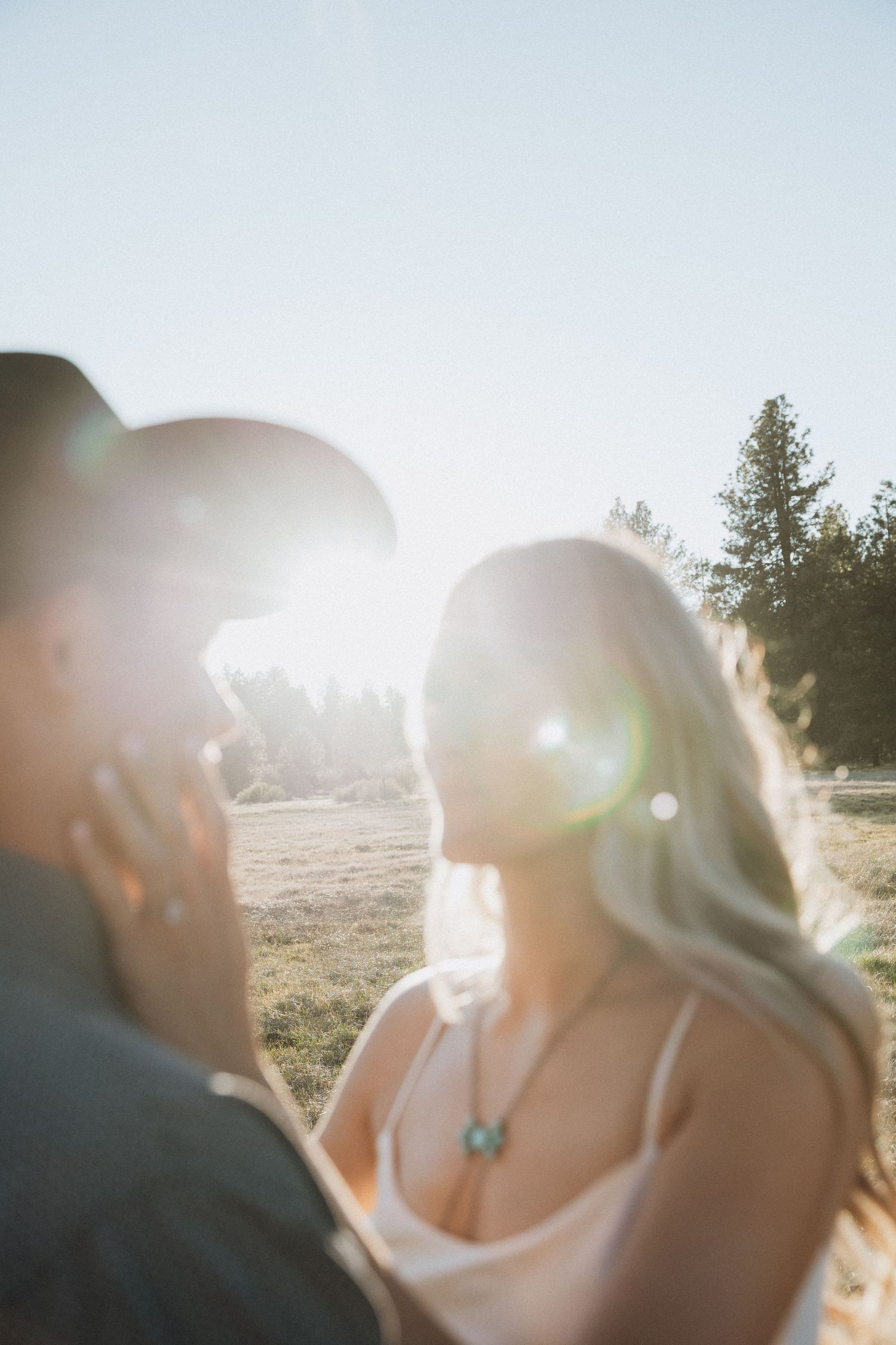 Couple sharing a romantic moment outdoors with golden sun flare, woman wearing white dress and turquoise necklace.