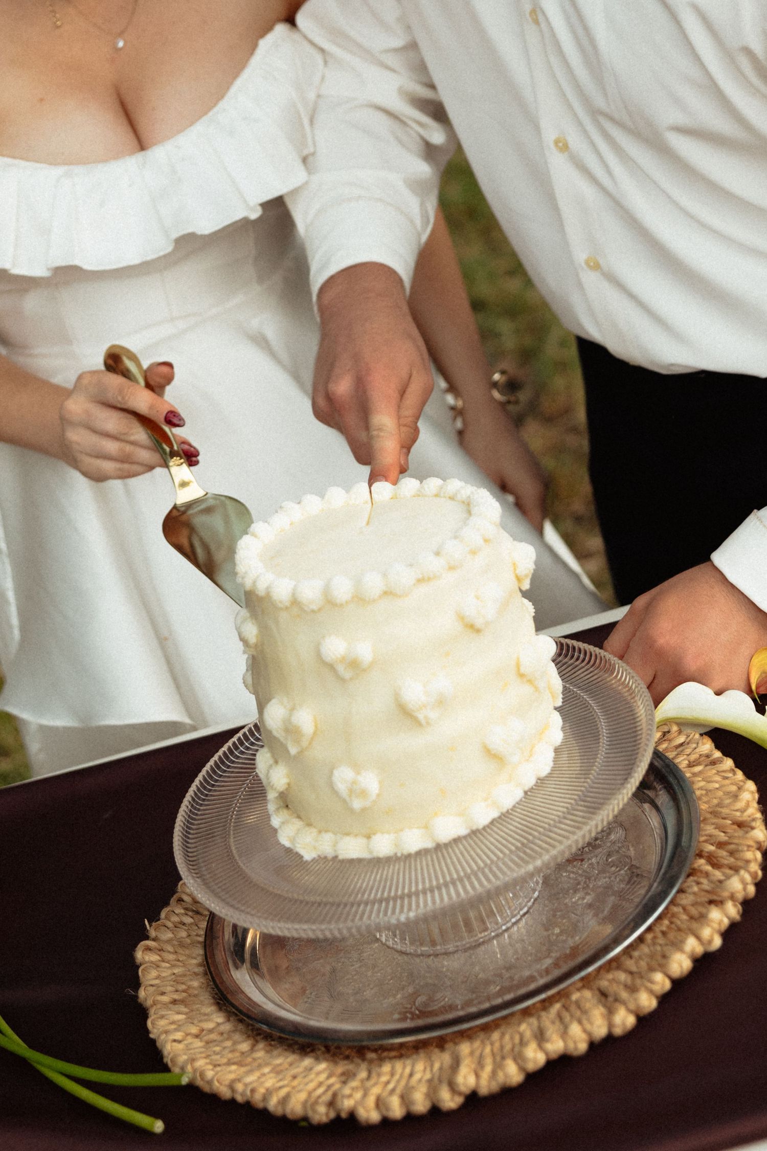 Bride and groom cut a elegant white two-tier wedding cake decorated with pearl dots and heart details.
