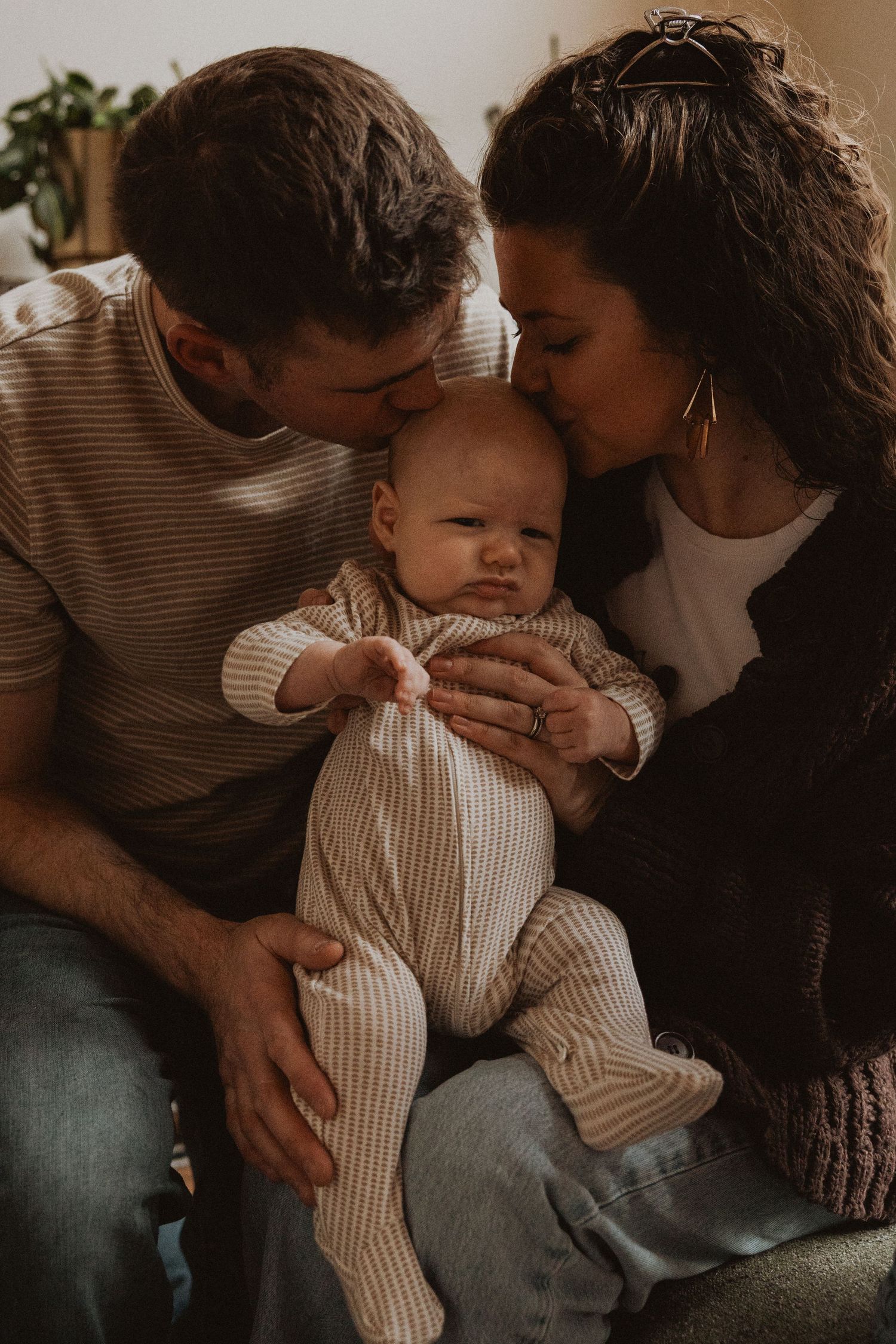 Loving parents both kissing their newborn baby on the cheeks in a warm home setting.