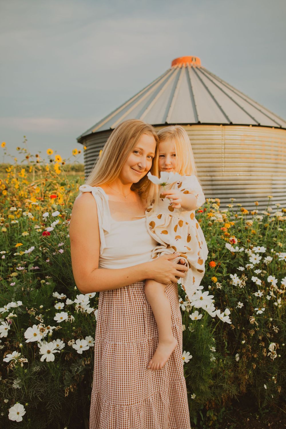 Family photos taken in a flower garden with grain silos in the background during golden hour.