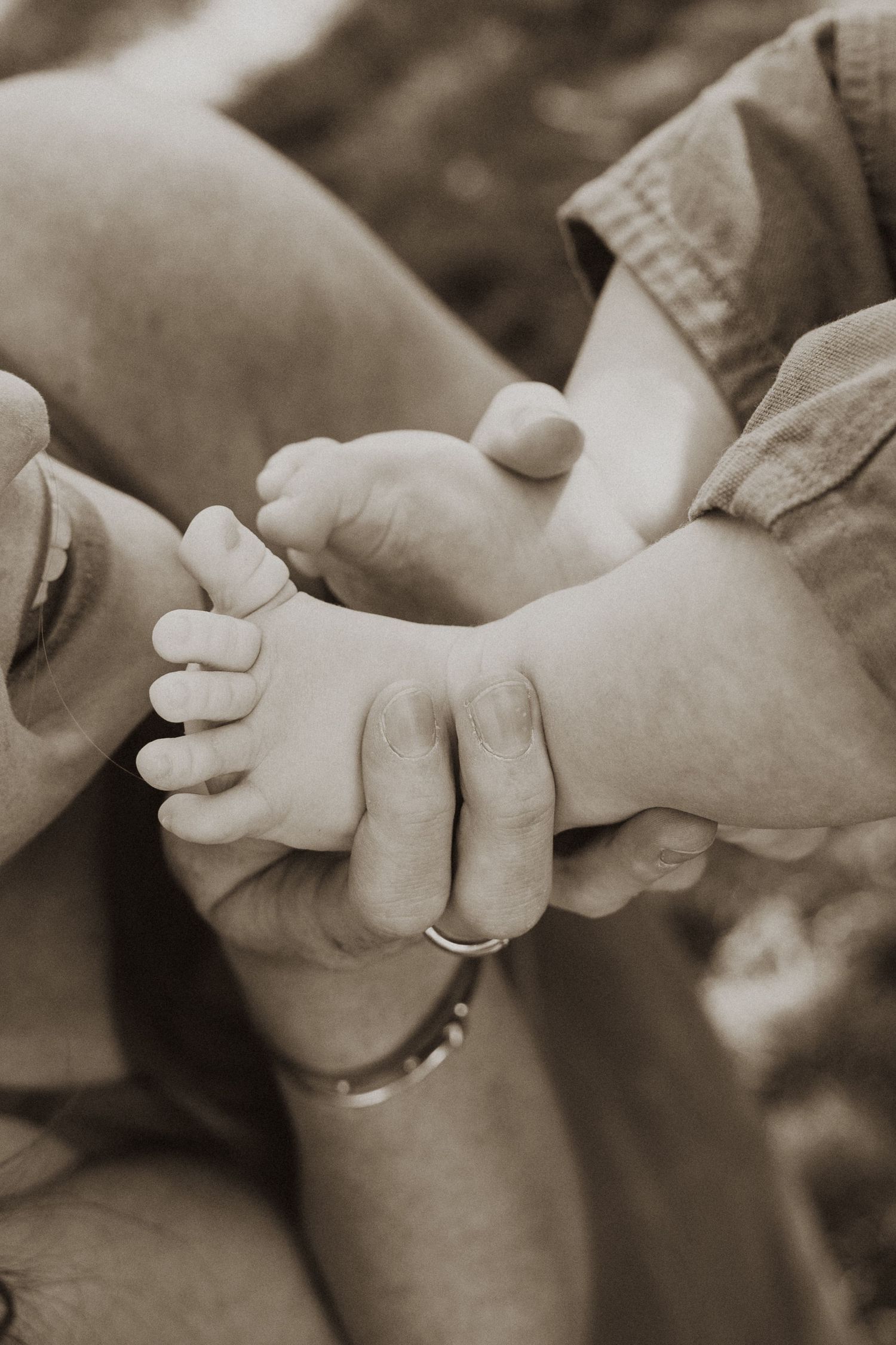 Sepia-toned close-up of an adult's hands gently cradling a baby's tiny feet, symbolizing parental love.