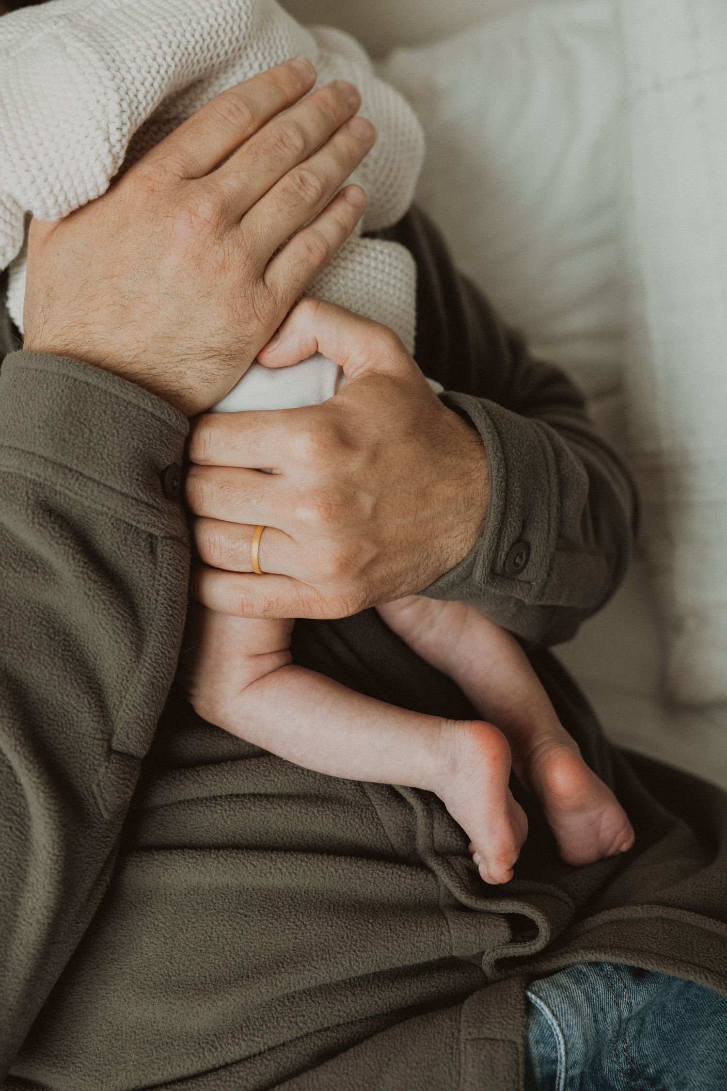 Close-up of parents holding a newborn baby, with one parent wearing a gold wedding ring, cradling tiny infant feet.