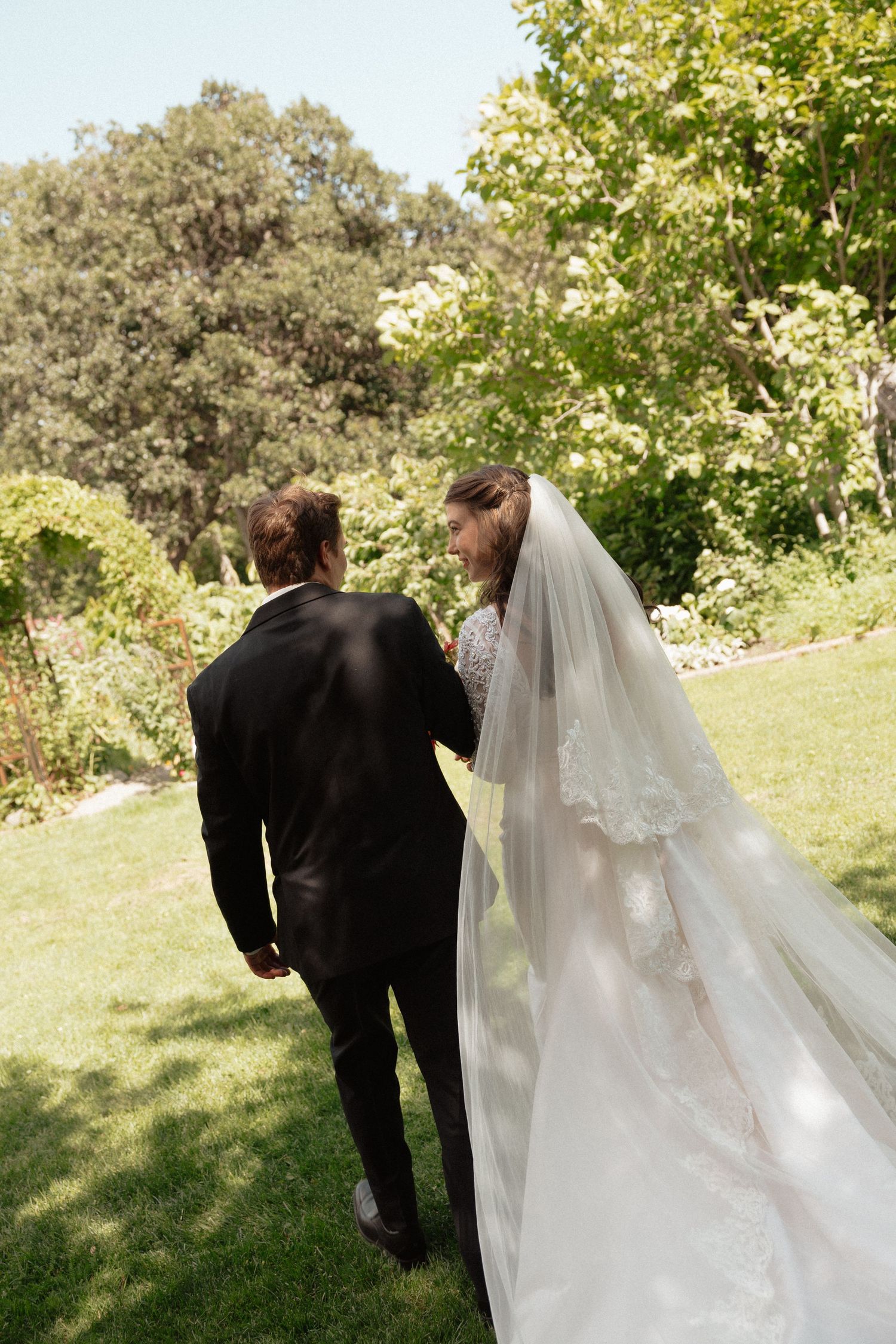 Bride and groom walking hand in hand through a lush green garden on their wedding day.