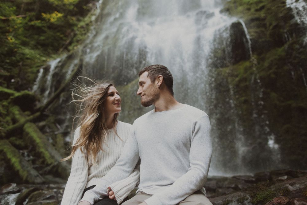 Couple in light colored sweaters sharing tender moments in front of a cascading waterfall.