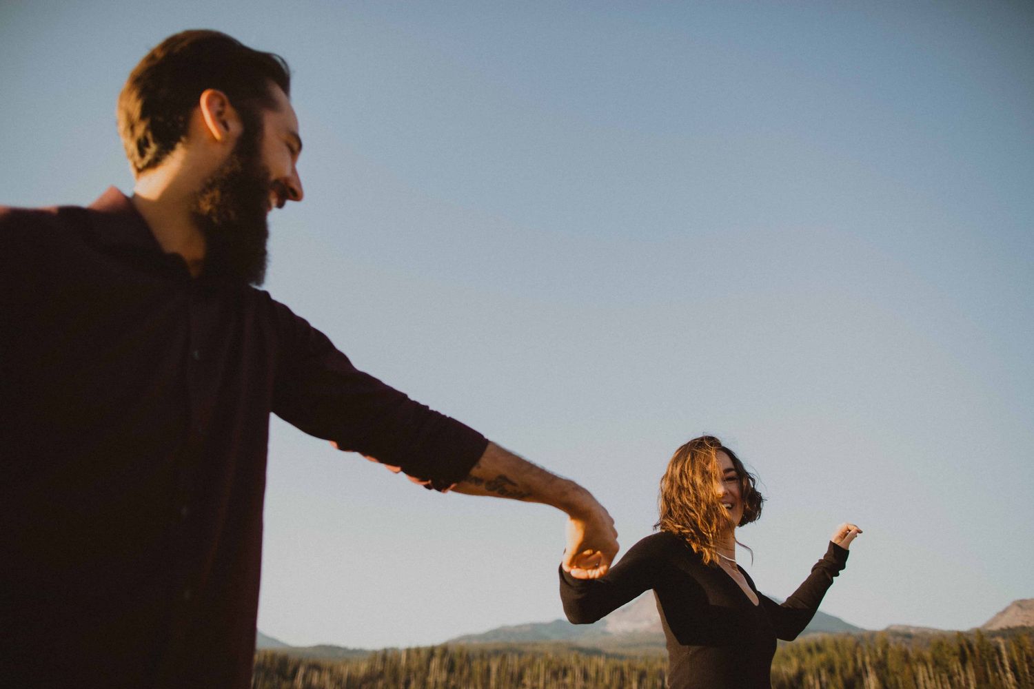A couple embraces in a golden field at sunset creating a romantic silhouette against the mountainous backdrop.