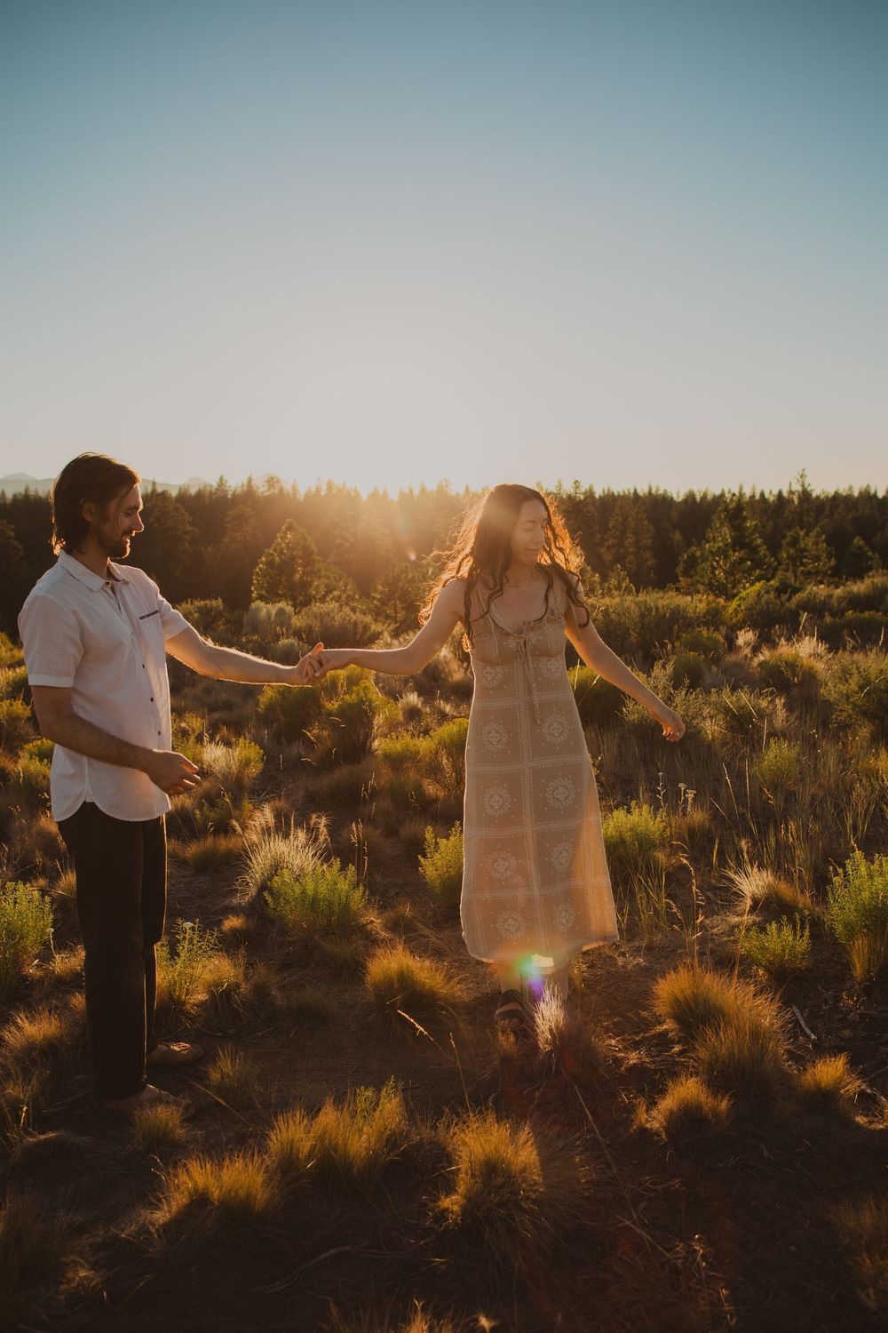 A couple dances playfully in a desert setting during golden hour.