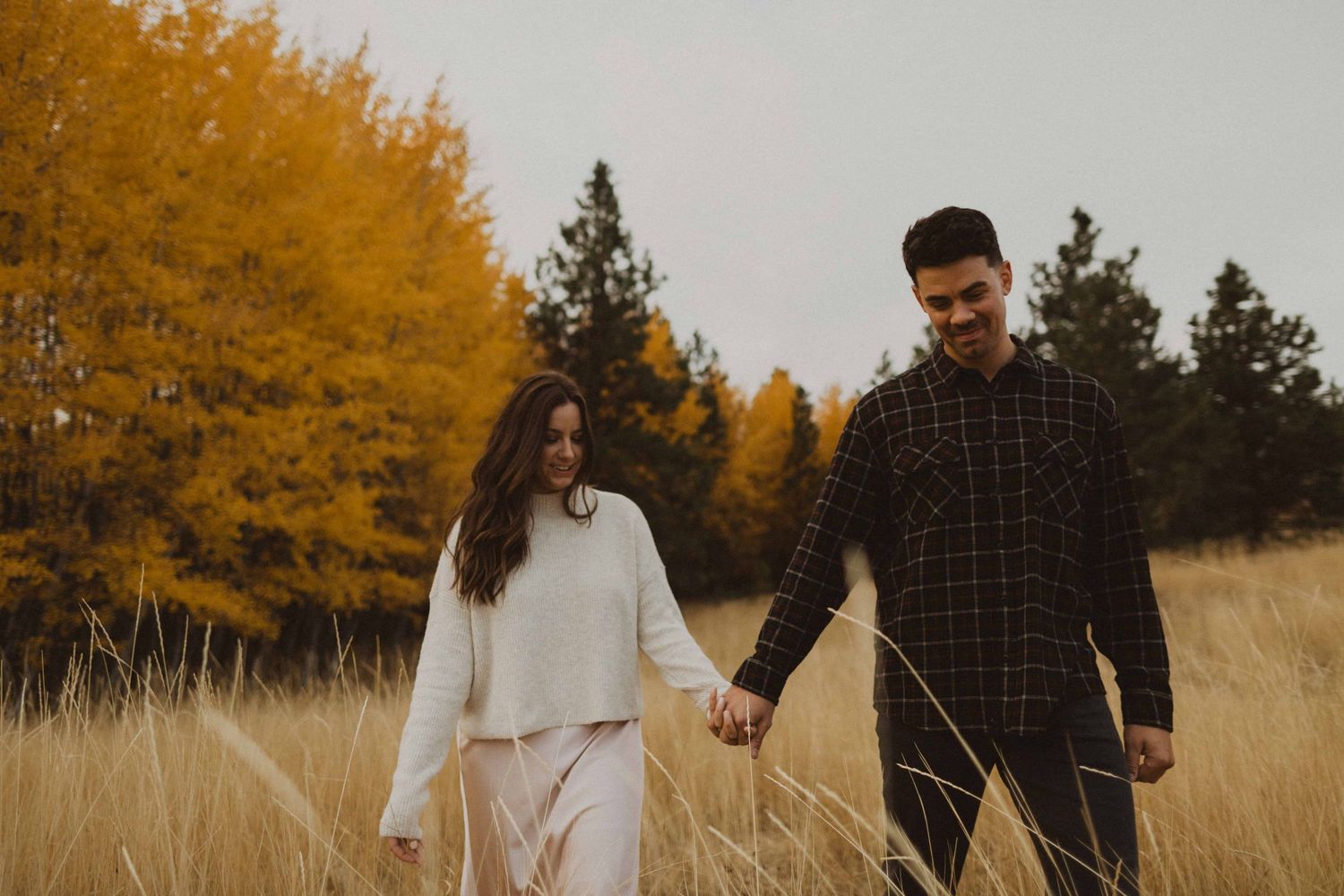 Two people share an intimate moment while walking through tall grass during sunset.