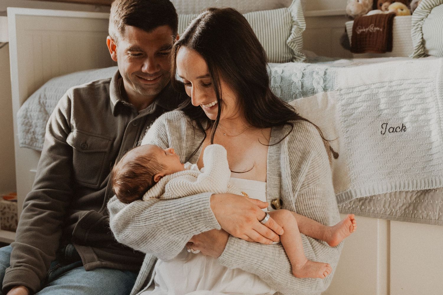 A couple smiles lovingly at their newborn baby named Jack in a cozy nursery setting.