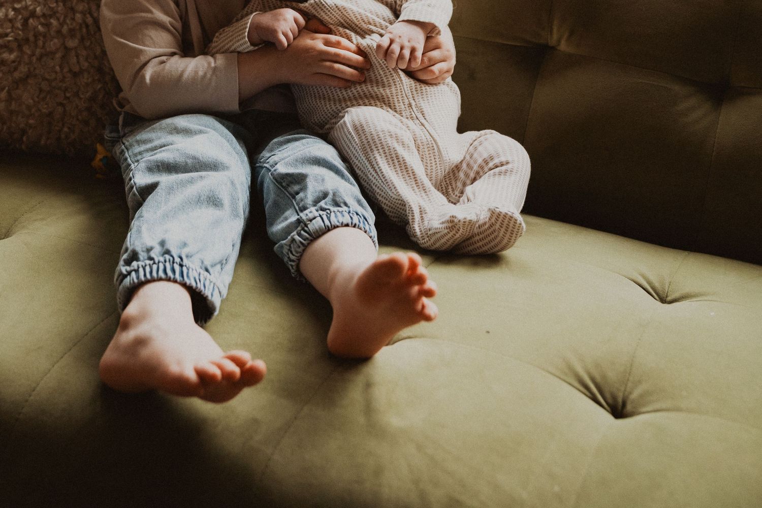Close-up of two young children's bare feet sitting together on a green couch.