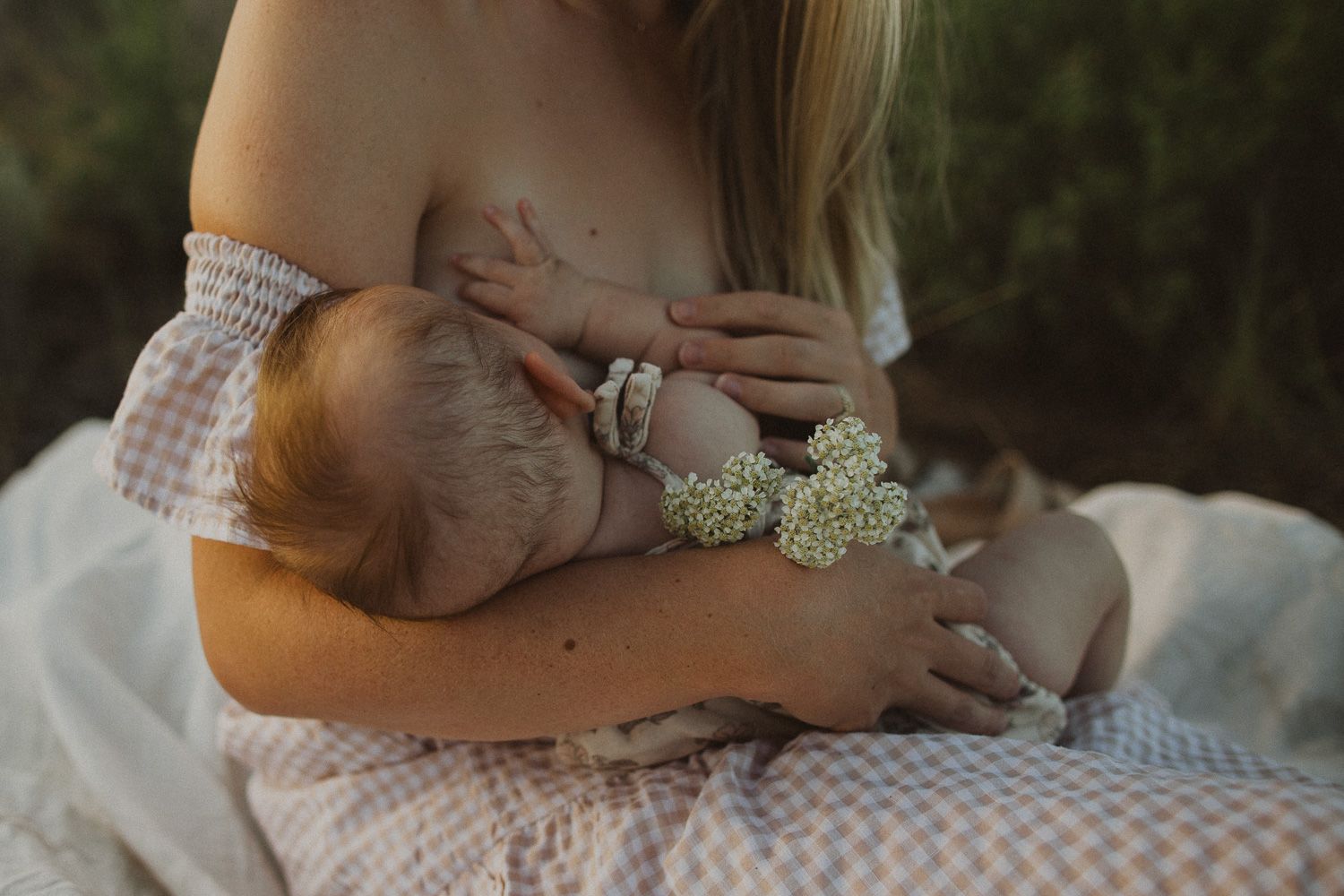 Close-up of nursing moment with baby and delicate white flowers against natural backdrop.