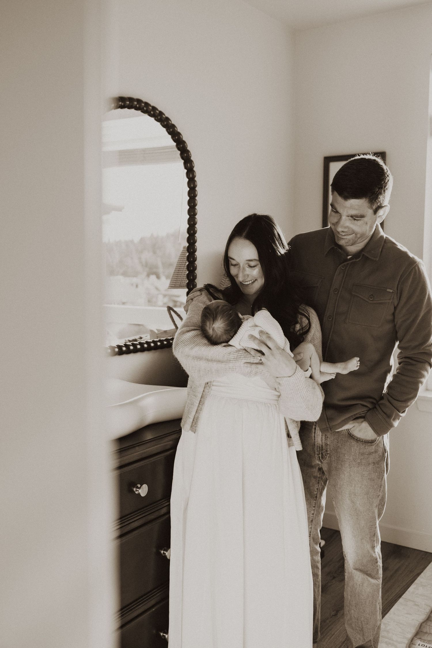 Sepia-toned photo of new parents cradling their newborn baby in a warmly lit bedroom.