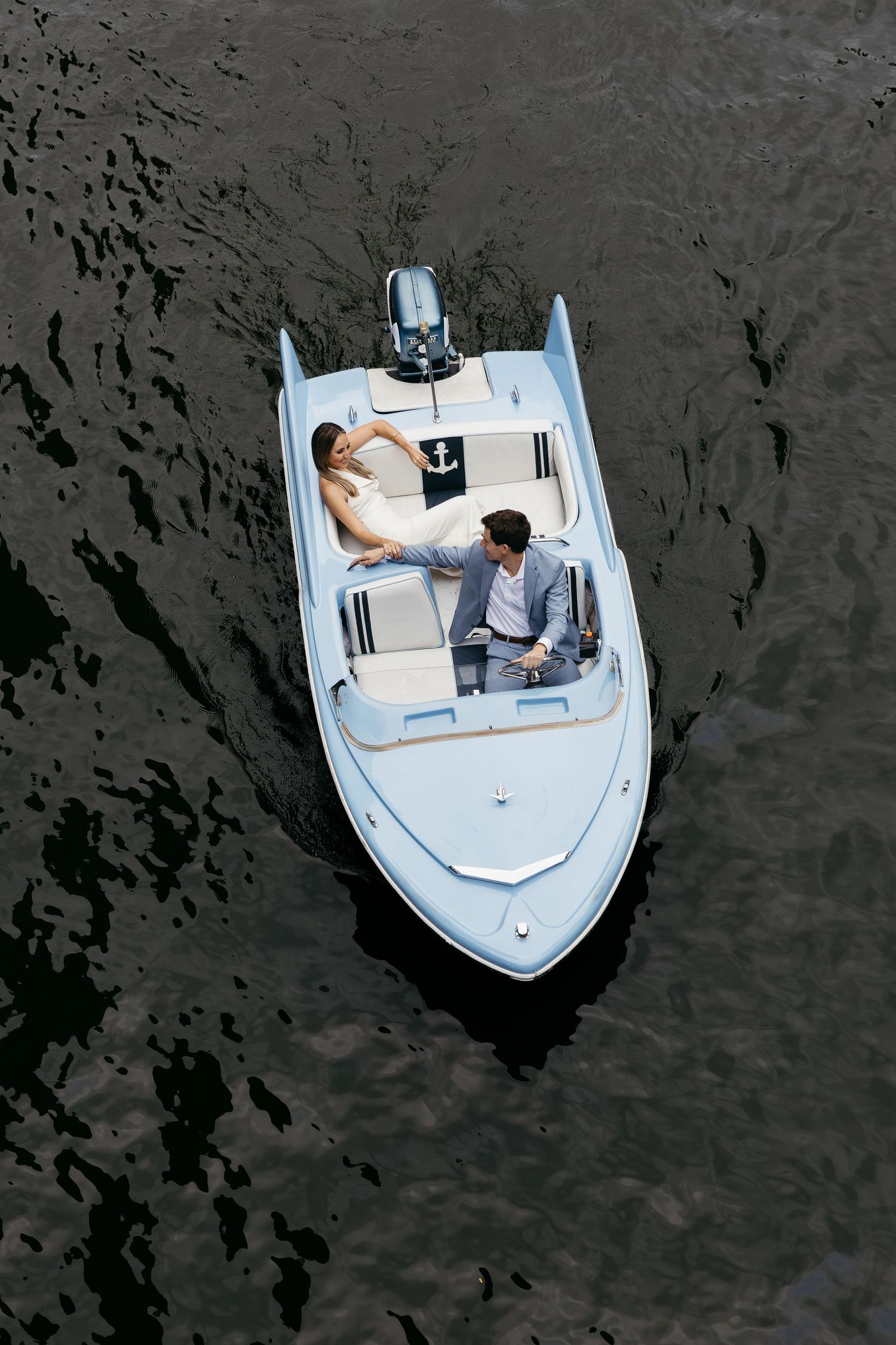 Aerial view of a couple relaxing on a white boat in dark waters.