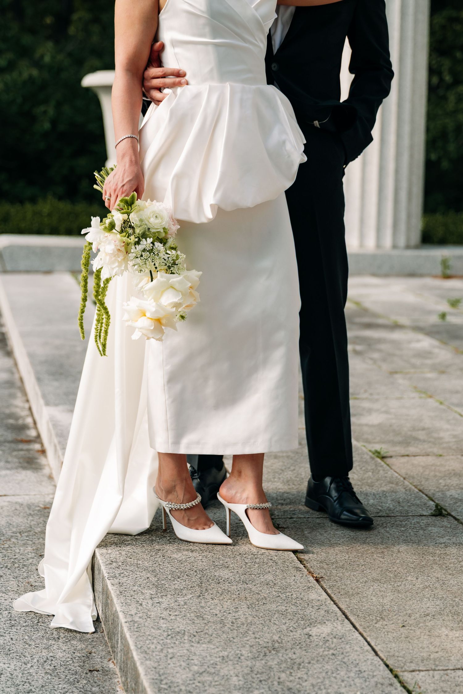 Close-up of bride and groom's feet on concrete steps with white dress and bouquet details.
