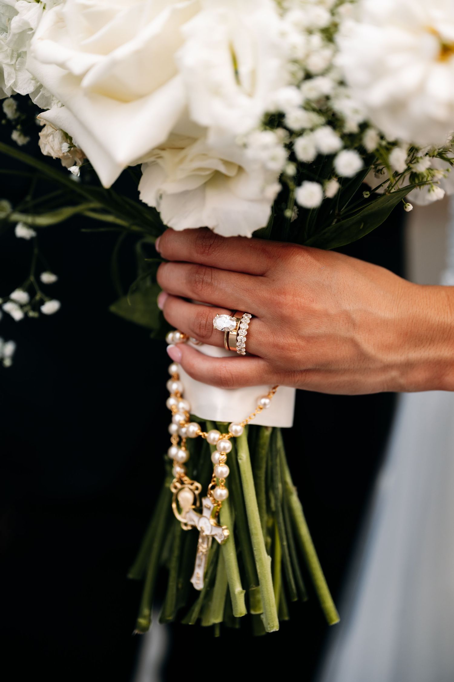 Close-up of bride's hands holding white rose bouquet with wedding ring detail.