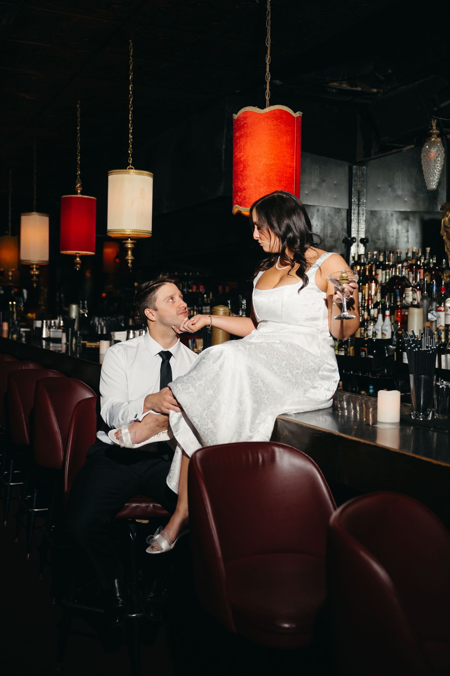 Couple enjoying romantic moment at dimly lit bar with red pendant lights.