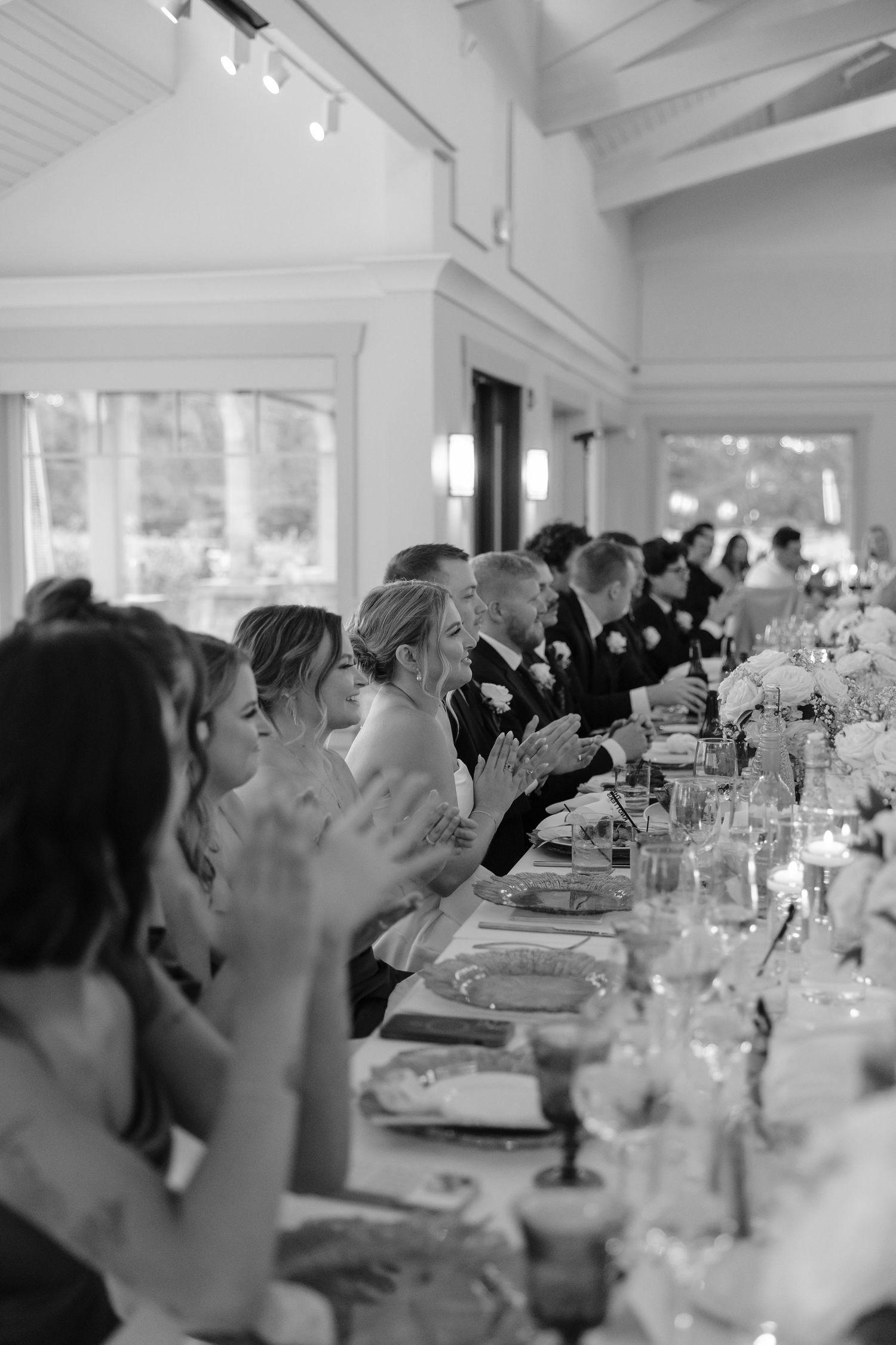 Wedding reception guests seated at elegant tables raise their glasses for a celebratory toast.