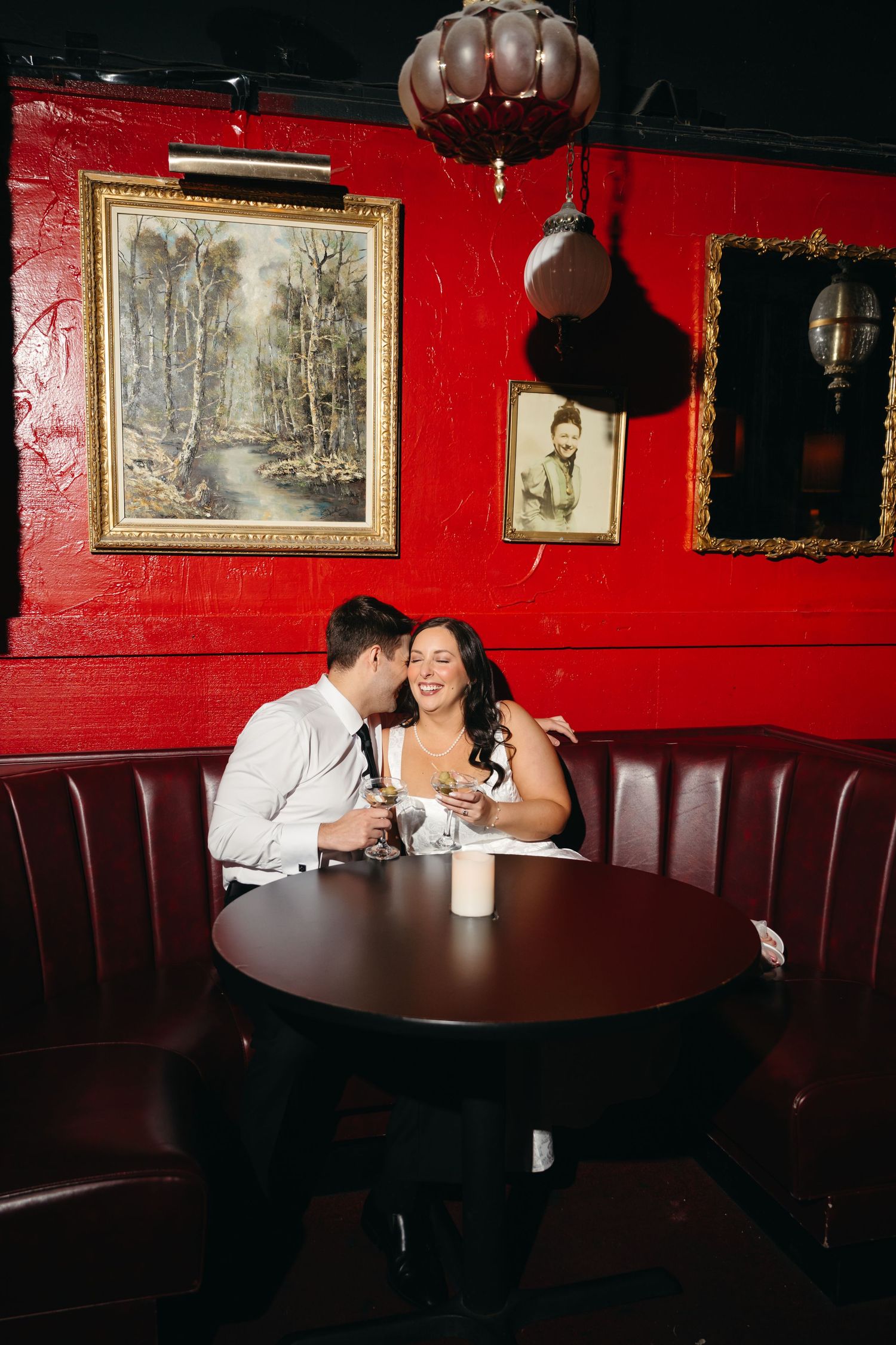 Couple sharing intimate moment in red-walled restaurant booth with vintage artwork.