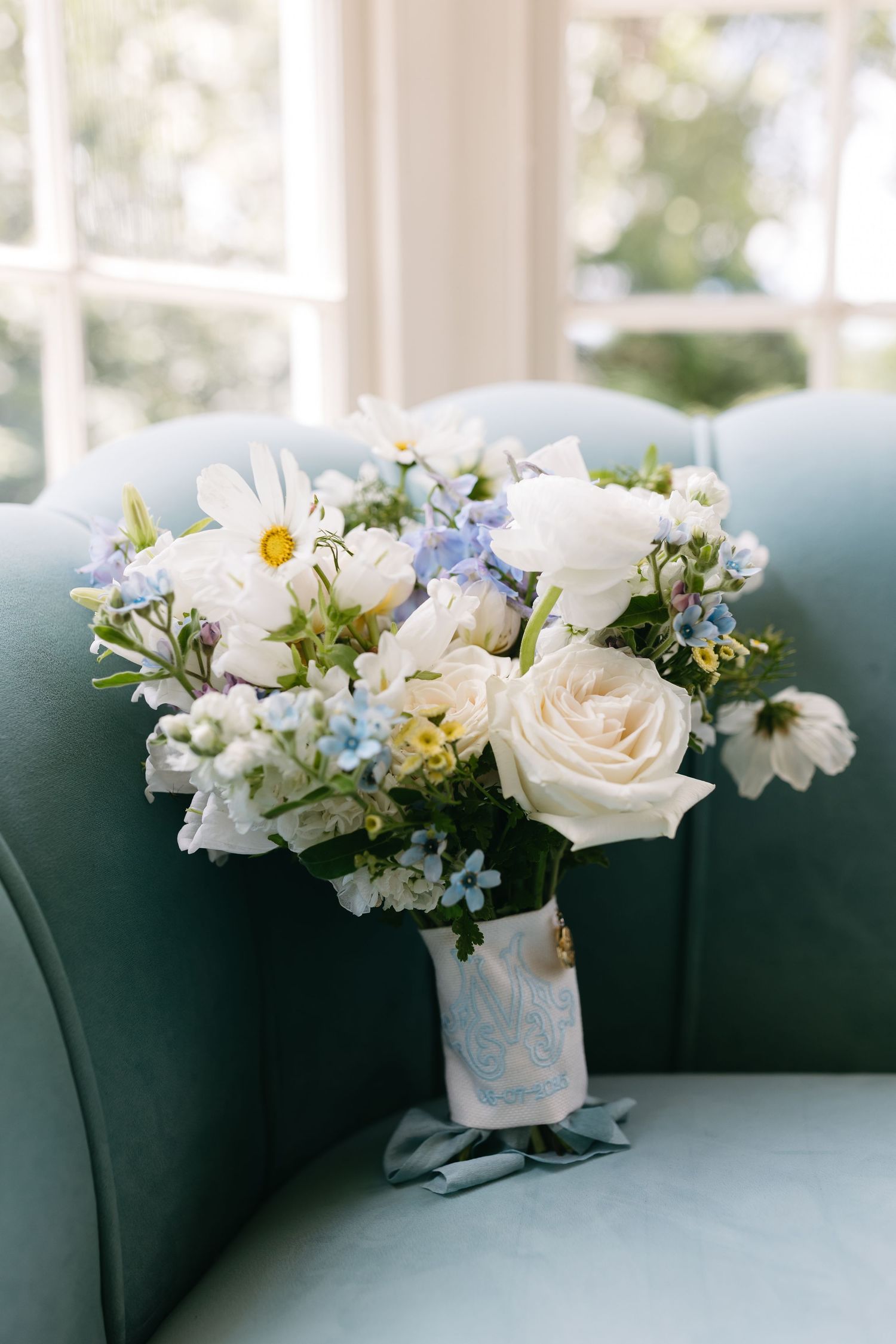 White and blue floral arrangements displayed along a teal colored couch.