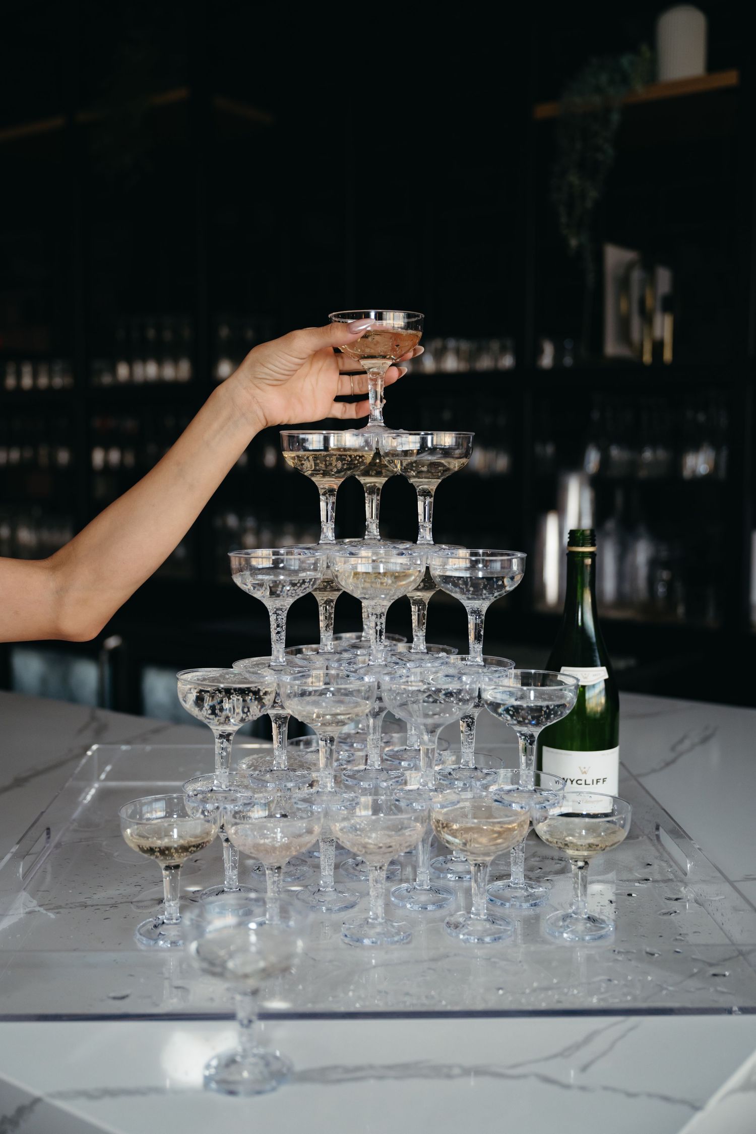 Champagne tower being built with coupe glasses as someone pours from the top.