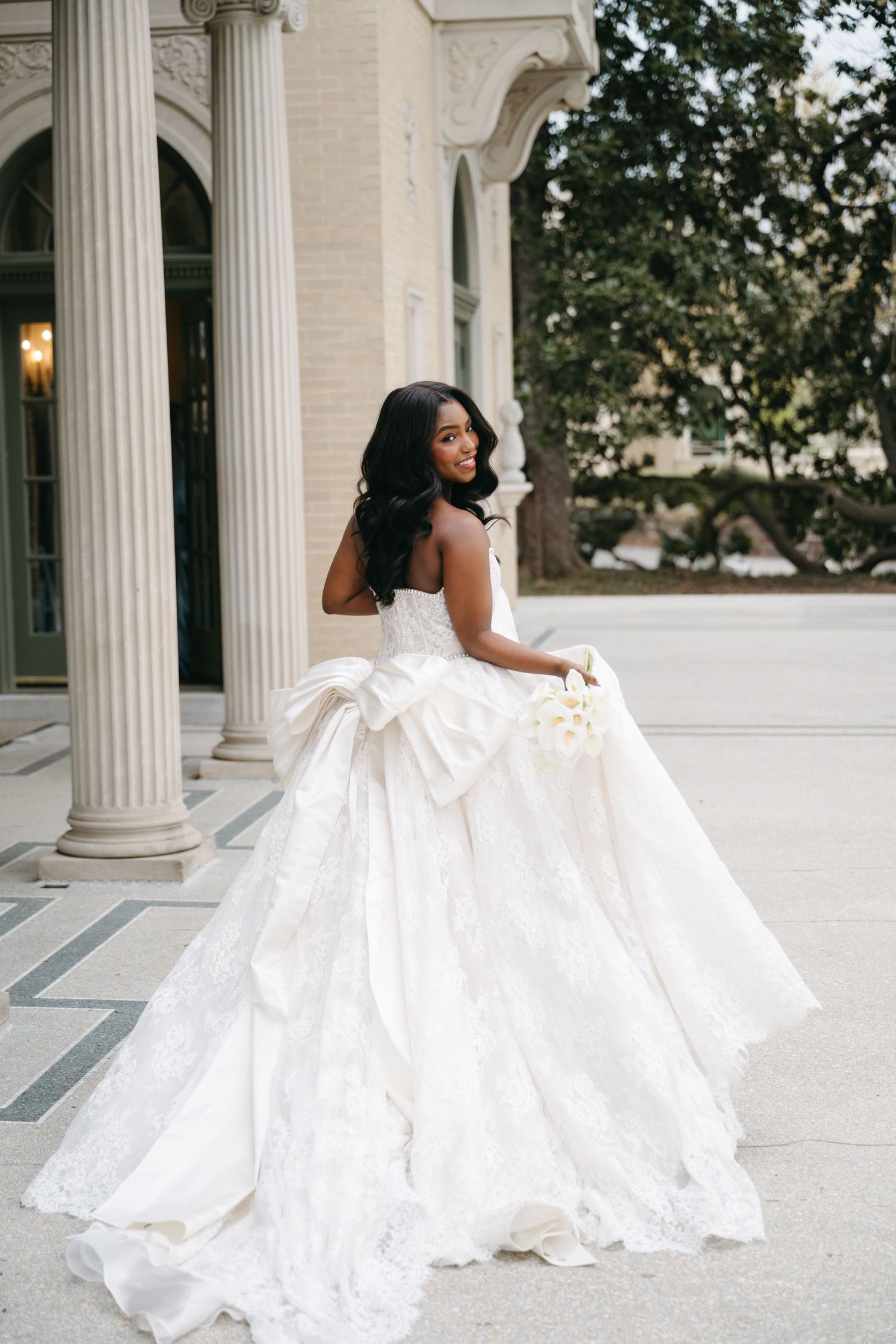 A bride in a ballgown wedding dress poses gracefully on a white columned terrace.