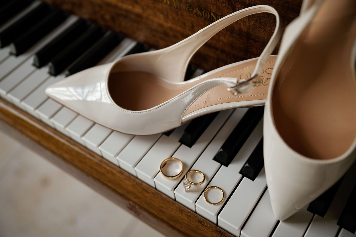 Elegant cream wedding shoes placed on piano keys with wedding rings.