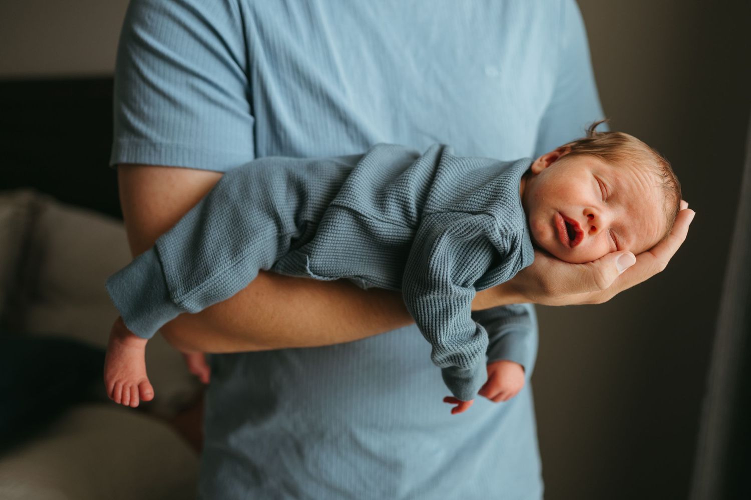 Parent in light blue shirt holding sleeping newborn baby in gentle embrace.