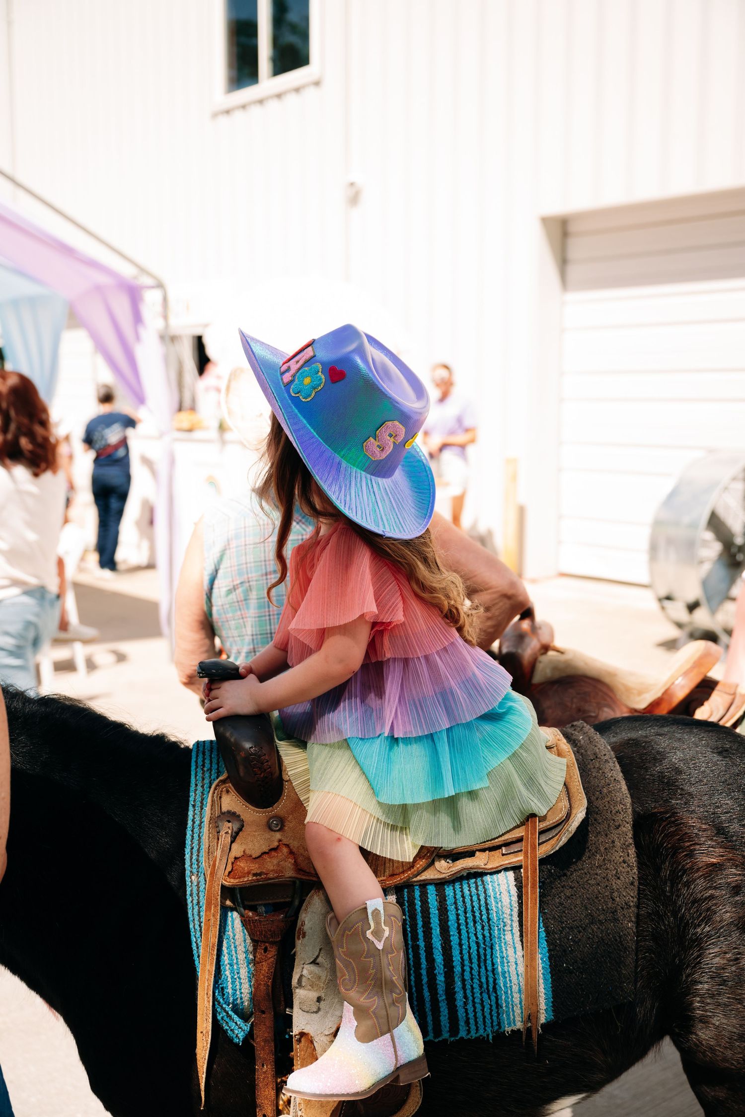 Child in pastel tutu and hat riding a pony at a birthday party.