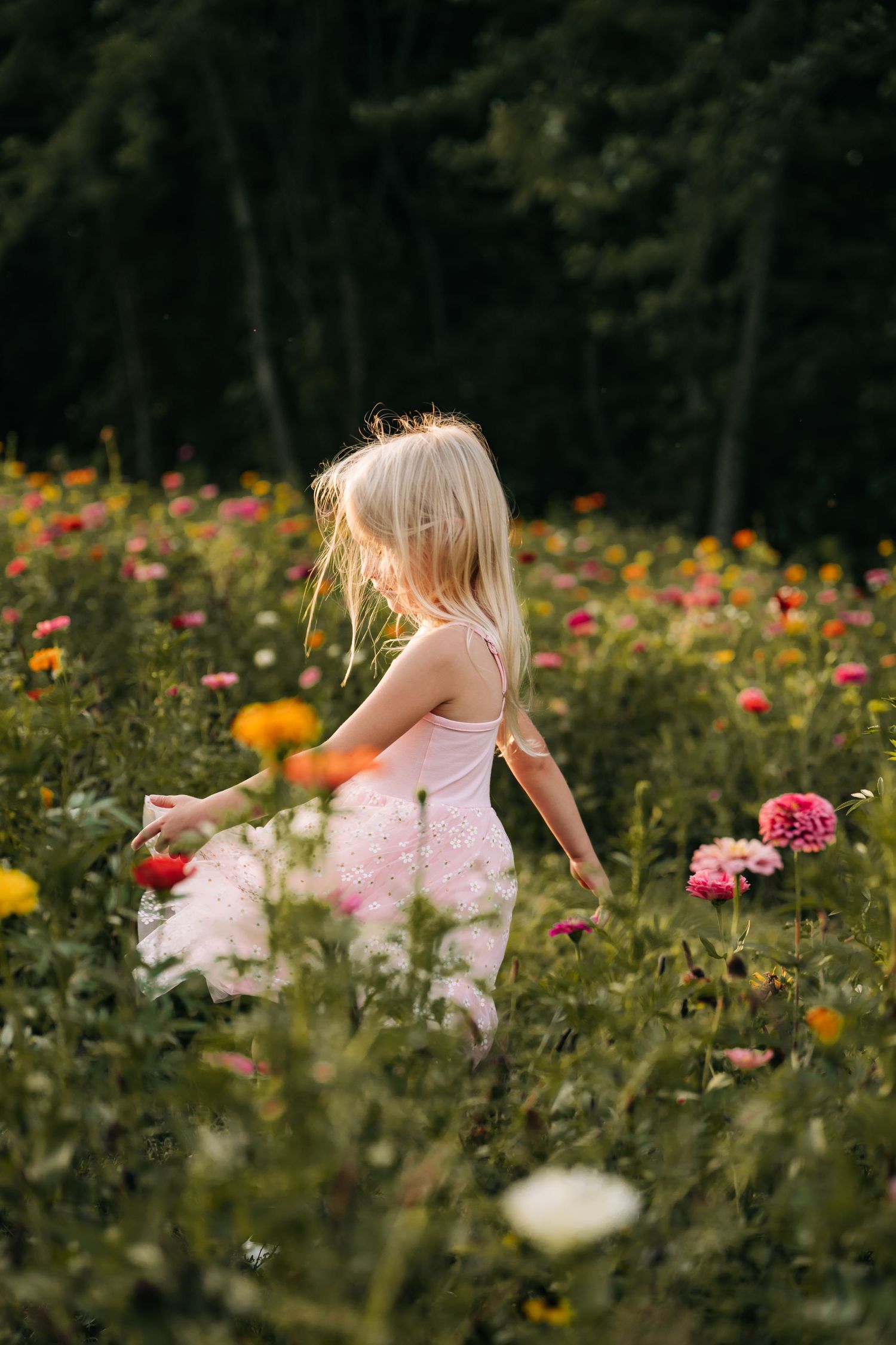 Young girl in pink dress running through a colorful wildflower garden.
