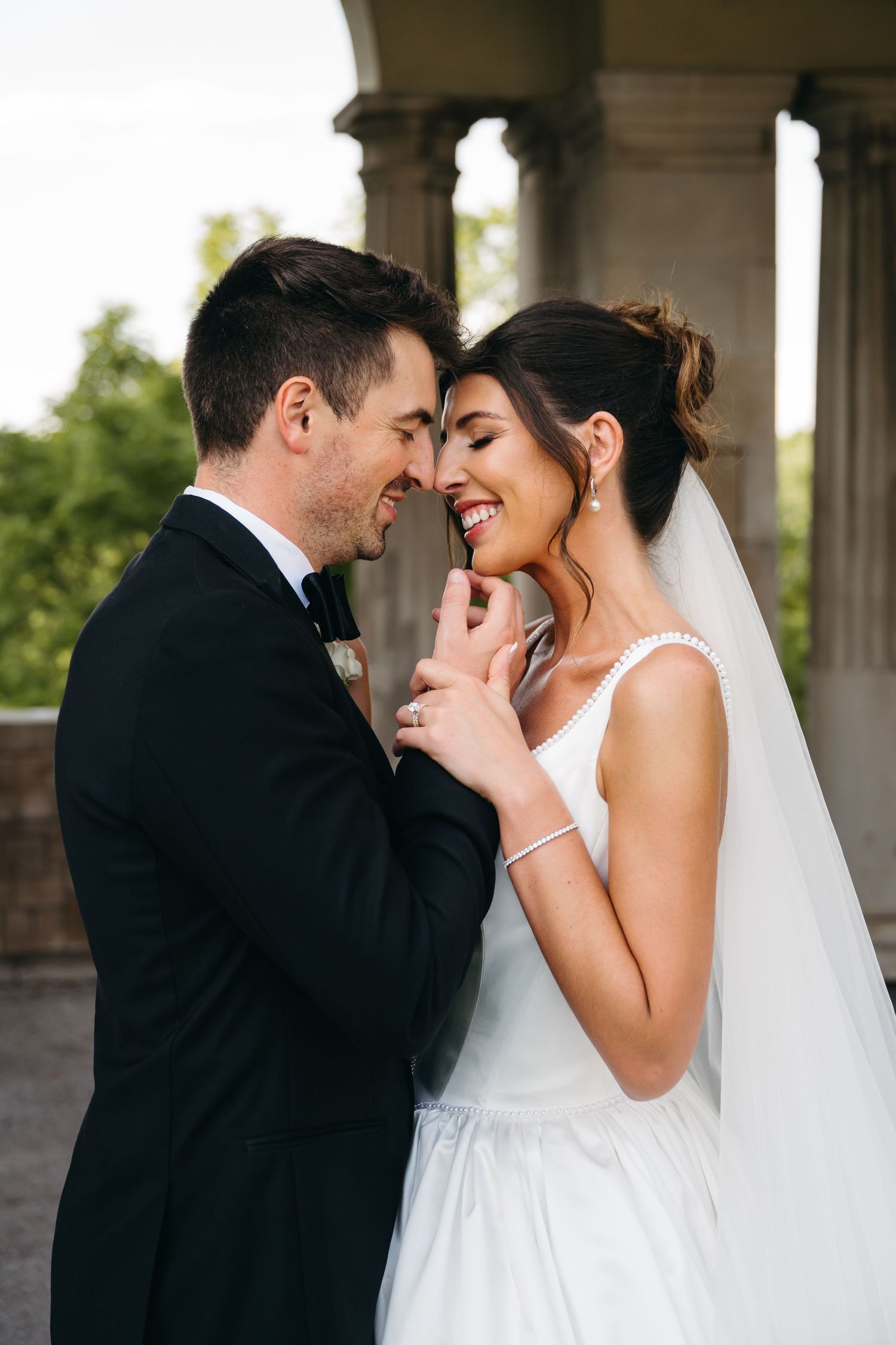 A romantic wedding moment captured of a bride and groom sharing an intimate embrace under a columned archway.