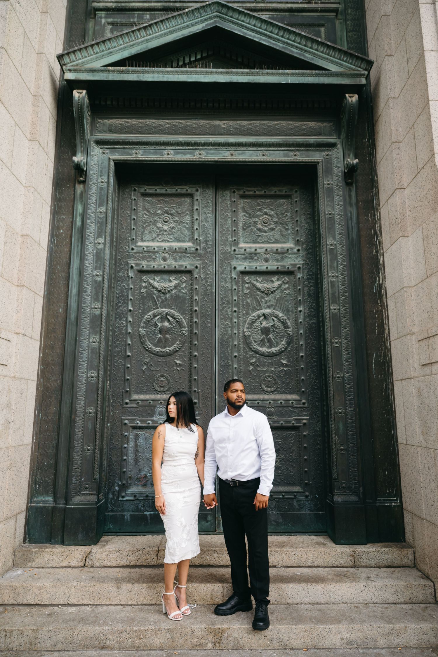 Couple standing in front of ornate metal doors on stone steps.
