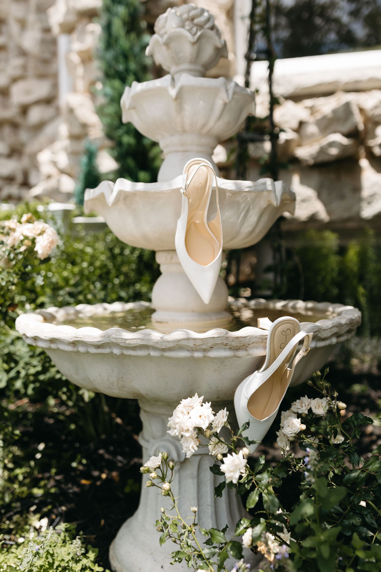 Ornate white stone fountain with delicate flowers in a garden setting.