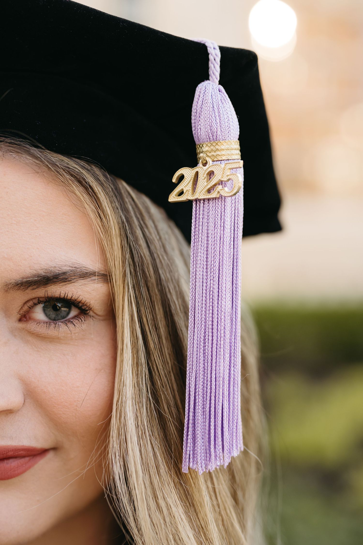 Close-up graduation photo detail showing purple tassel and 2023 charm against a blurred background.
