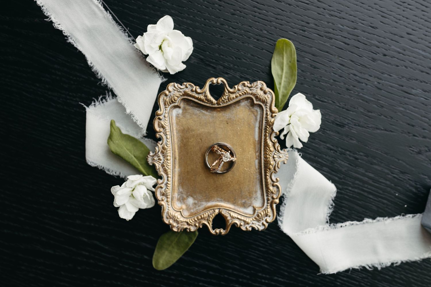 Wedding details with white flowers and vintage gold tray on dark surface.
