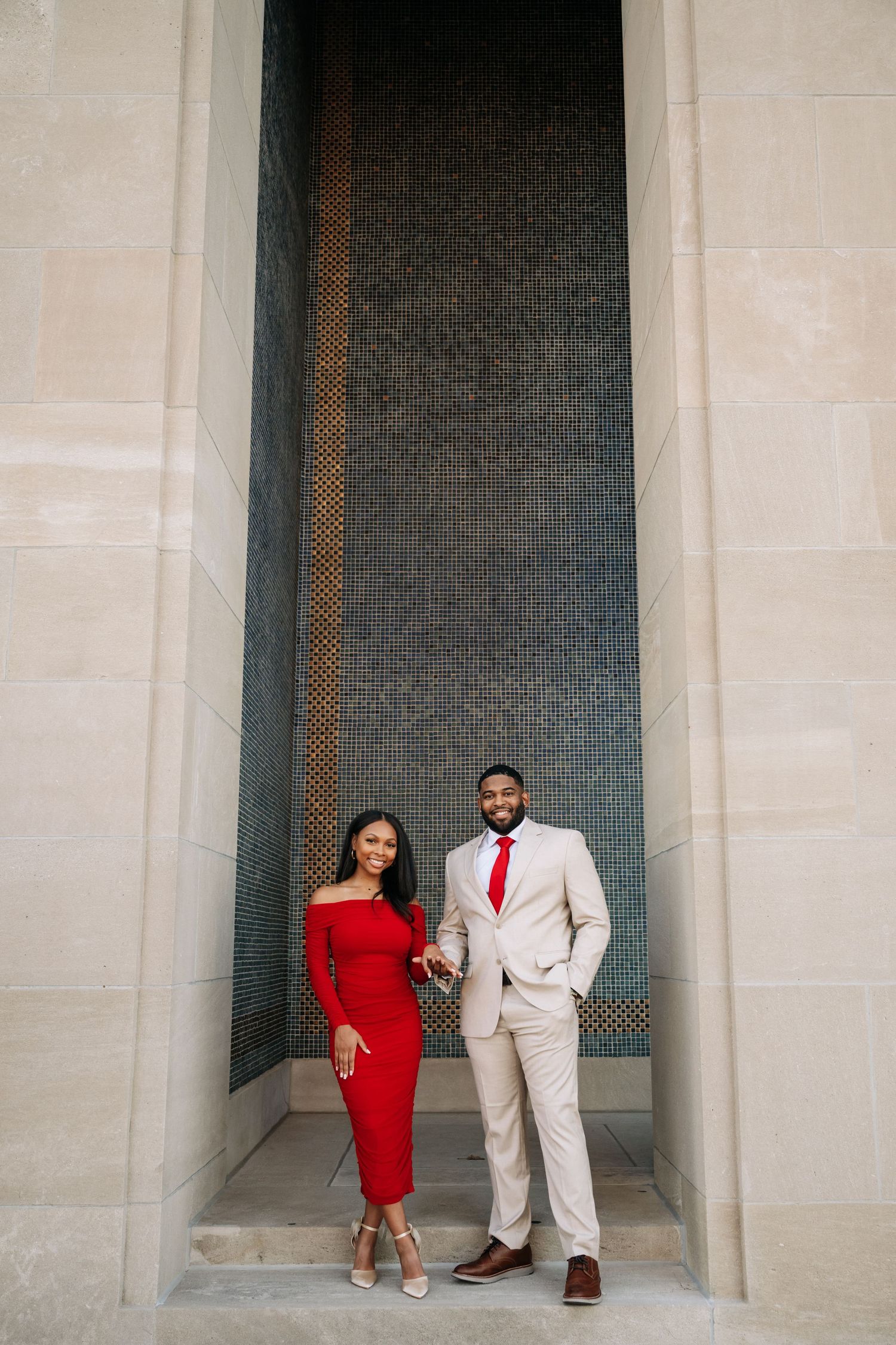 Couple in formal attire posing against stone wall alcove.