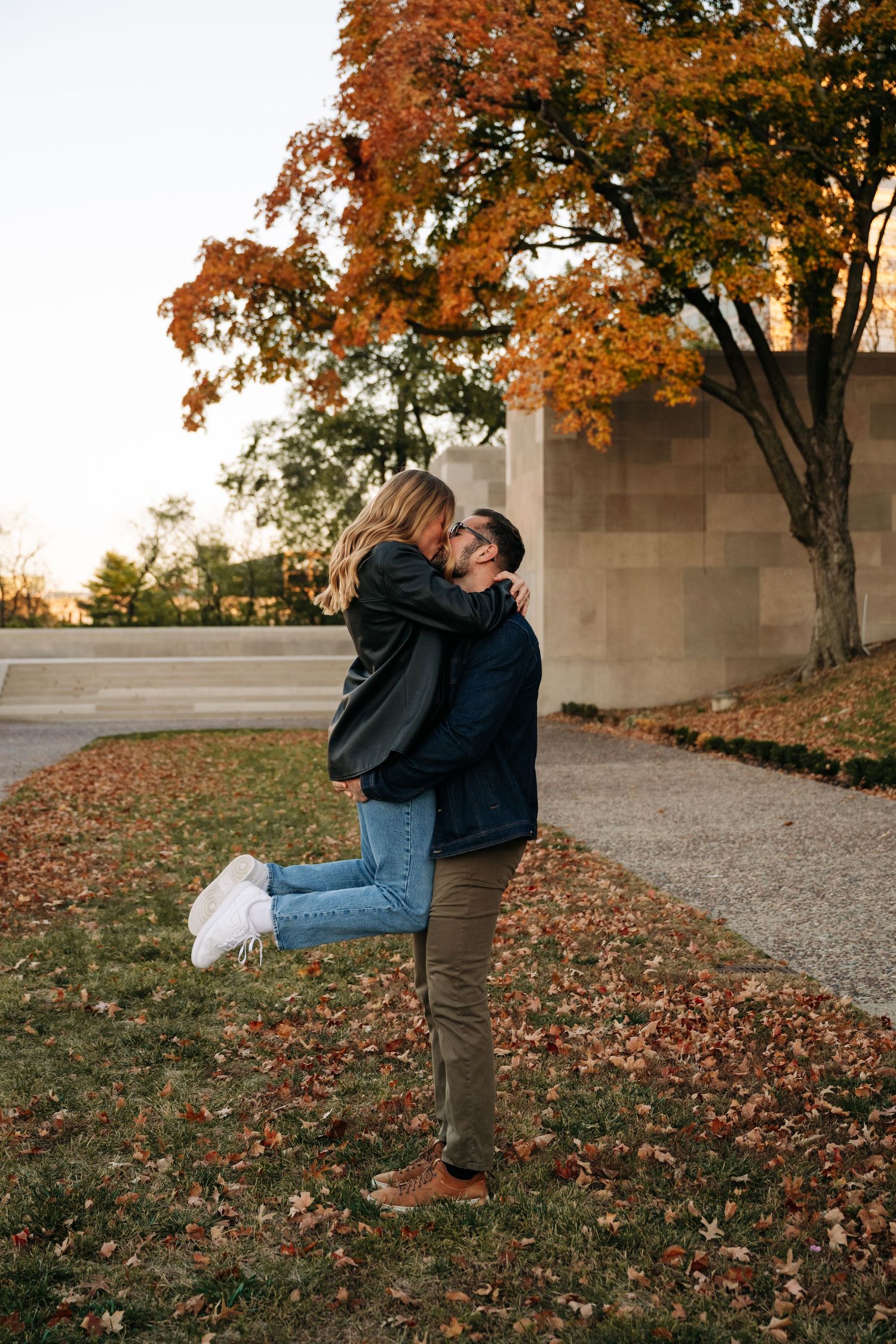 A couple shares a playful moment among fall foliage and fallen leaves.