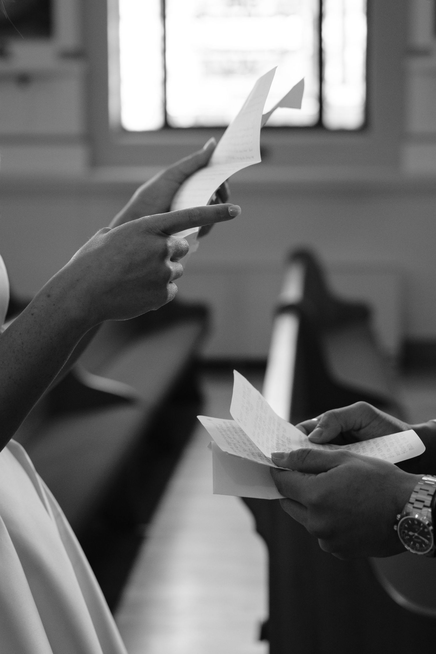 Black and white close-up of hands holding paper programs during a ceremony.