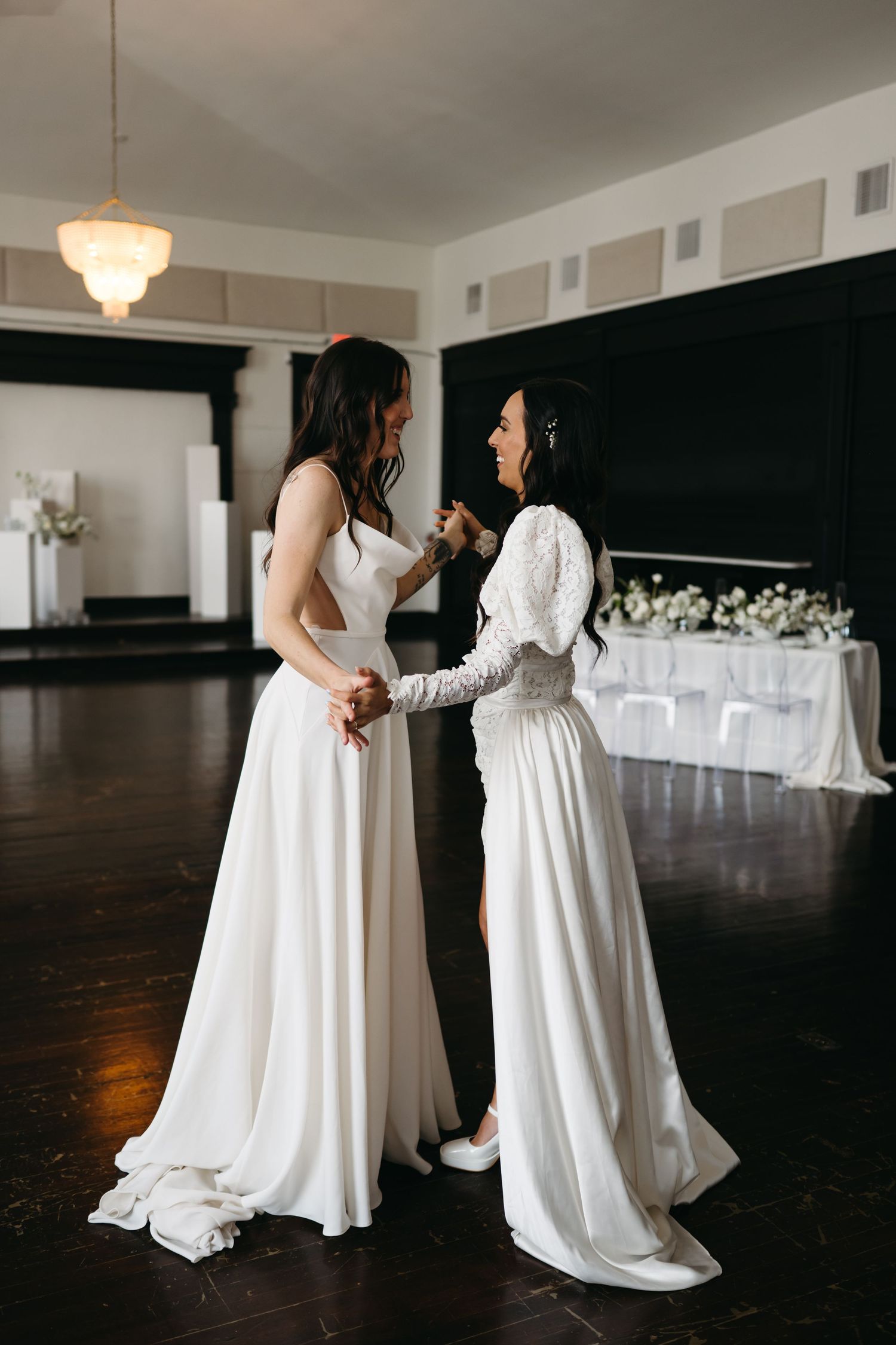 Two wedding dresses swirl during a dance in an elegant reception room.