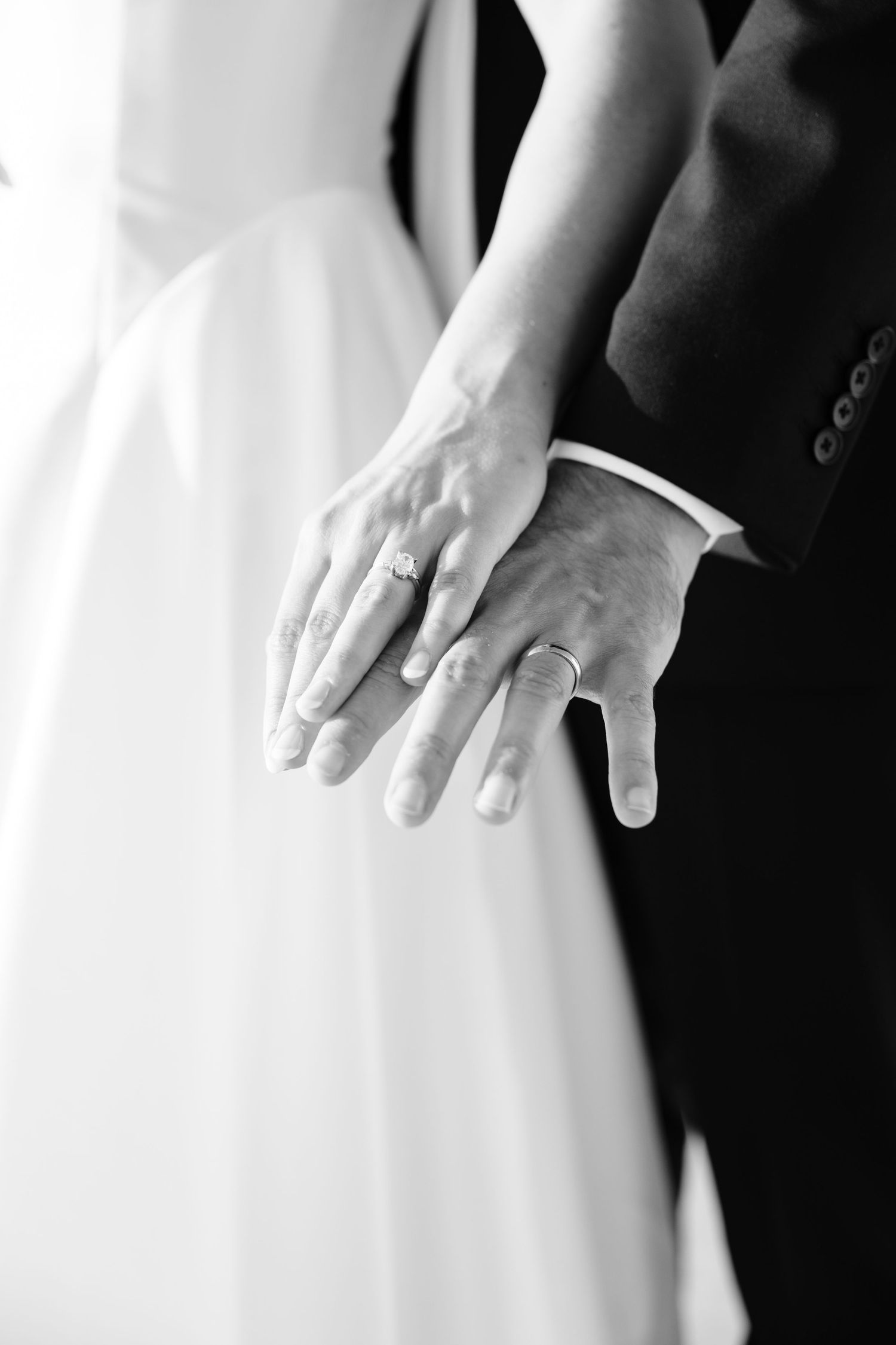 Close-up view of newlyweds holding hands showing wedding rings in black and white.