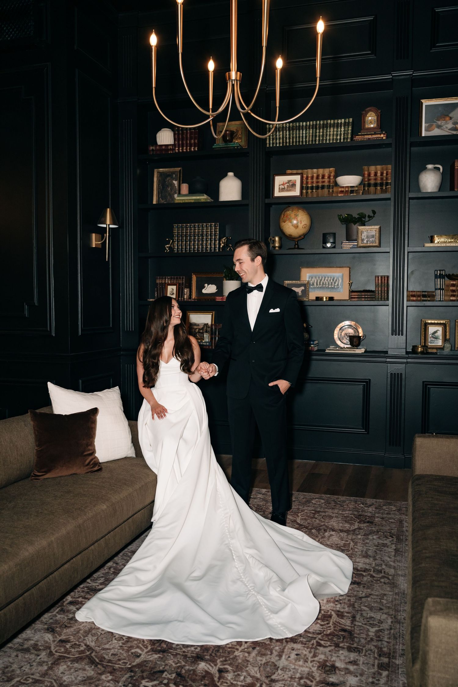 Elegant wedding dance in a dark room with chandelier and built-in bookshelves.