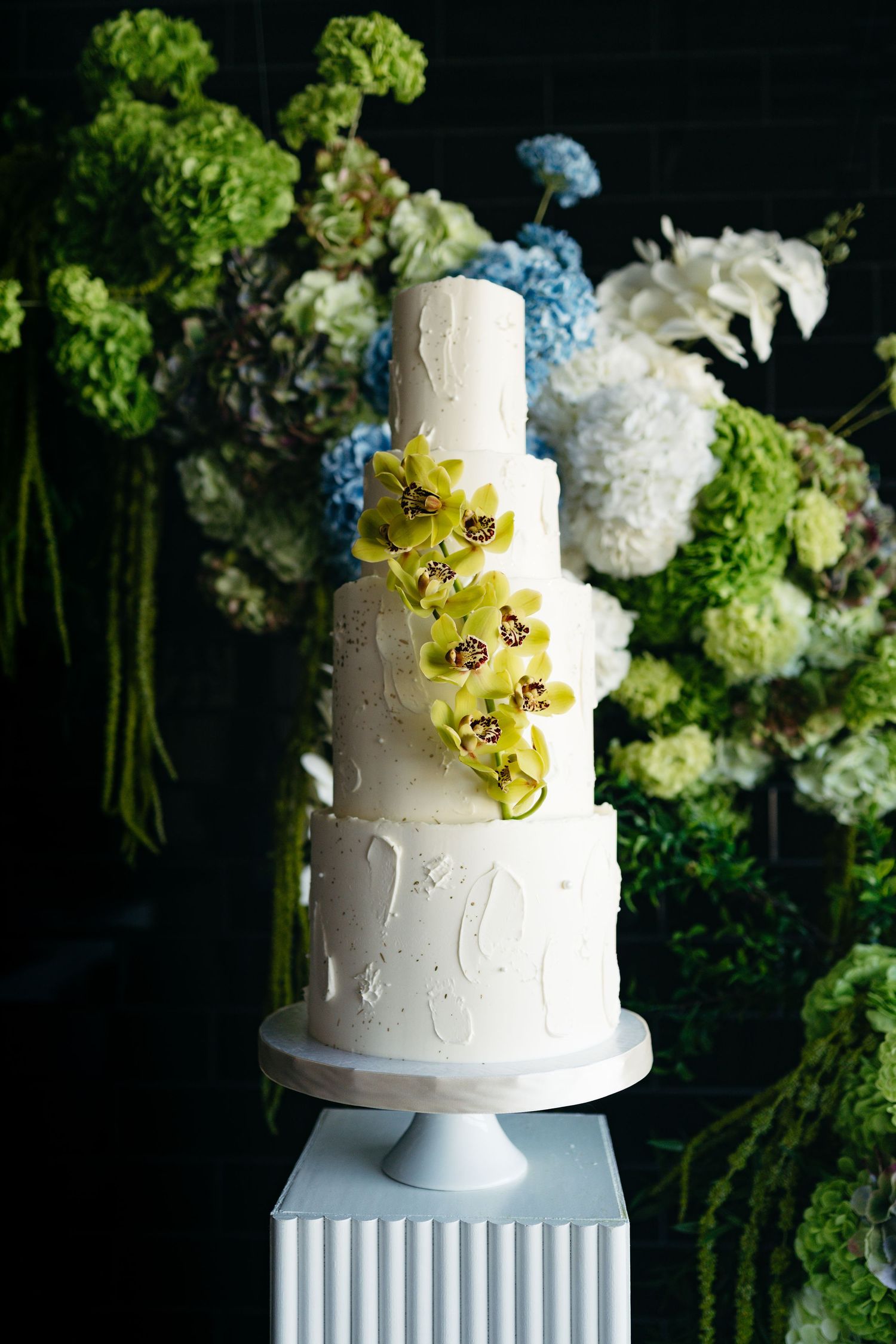 Elegant white wedding cake with yellow orchids and green hydrangea floral decorations.