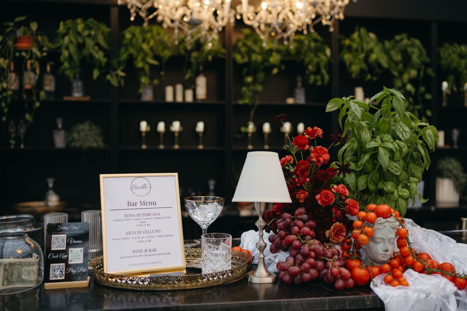 Elegant table setting with menu card, martini glass, crystal chandelier, fresh grapes and herbs in a dark moody atmosphere.