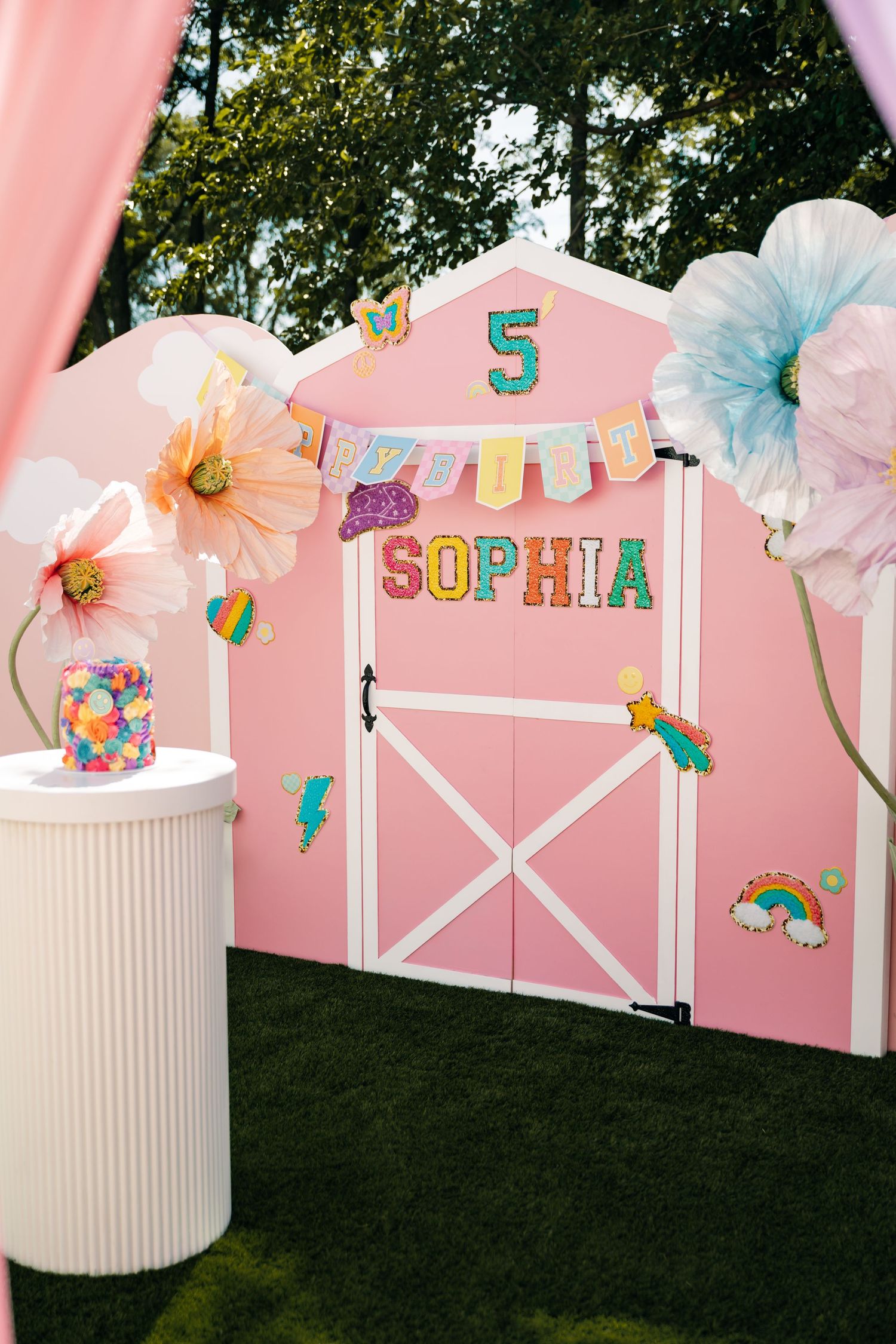 Pink and pastel decorated party backdrop with paper flowers and festive banners.