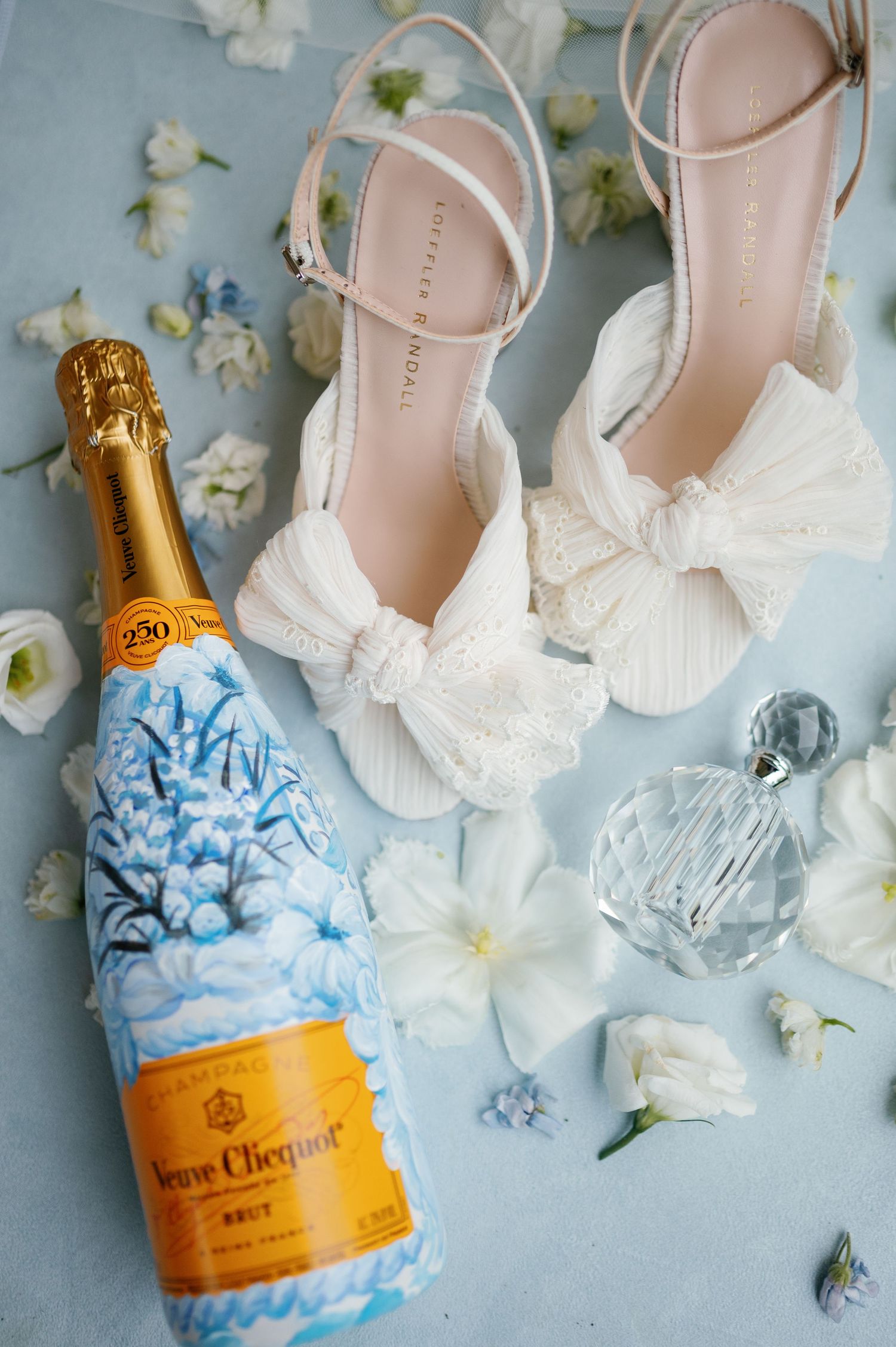 Wedding accessories including white shoes and champagne bottle decorated with blue hydrangeas.
