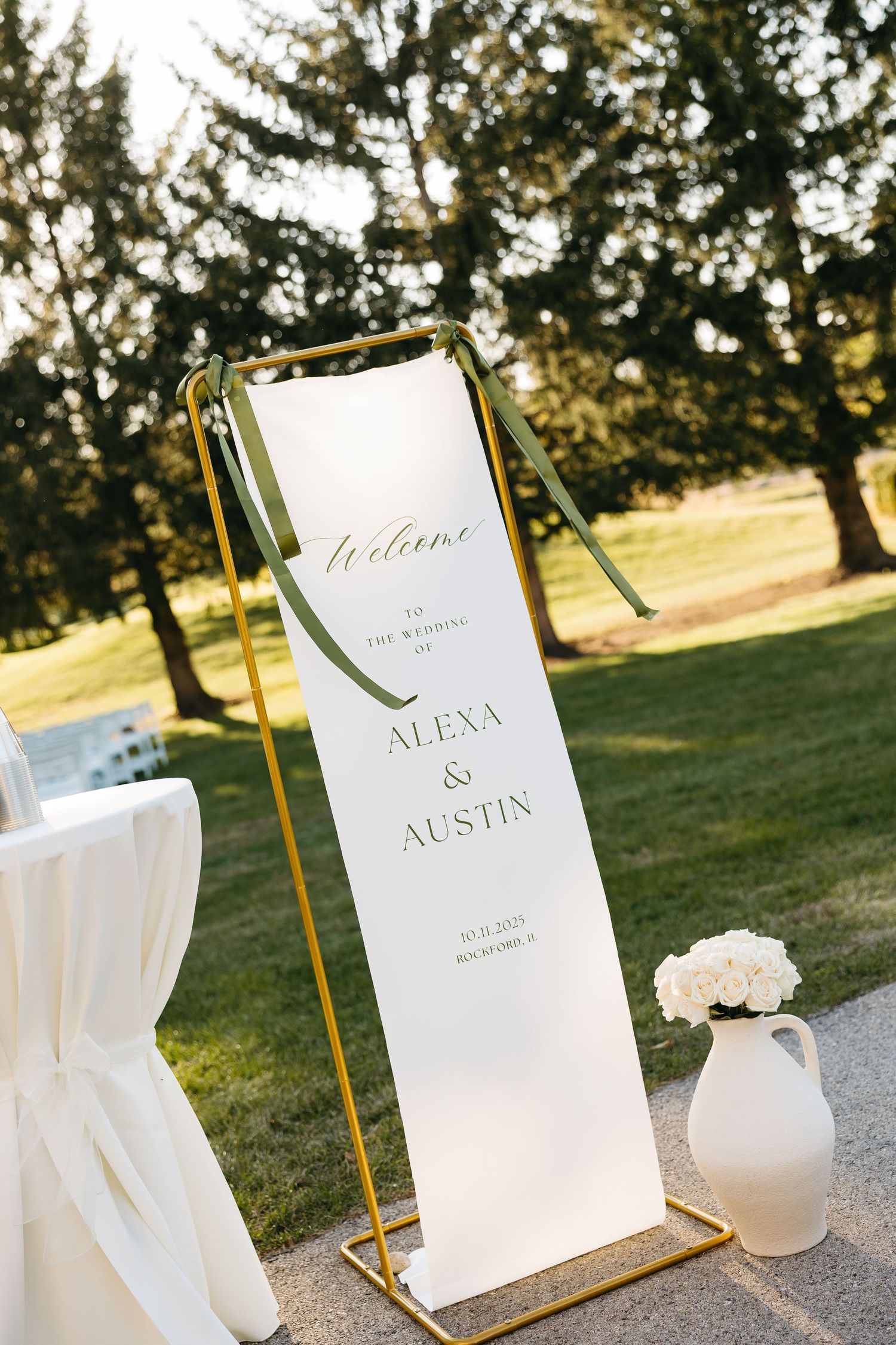 Elegant wedding welcome sign in gold frame with white florals outdoors.