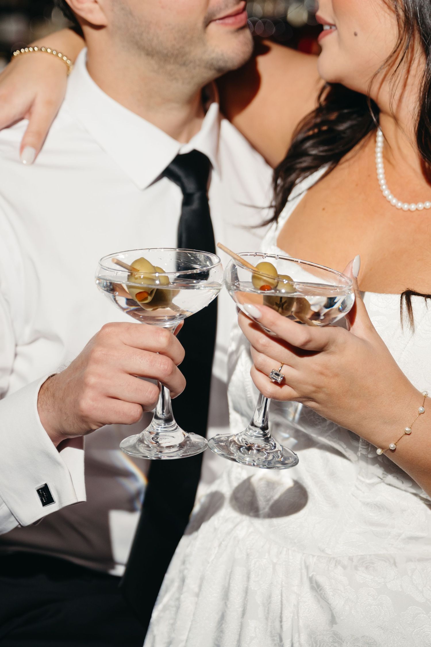 Close-up of martini glasses held by couple in formal wedding attire.
