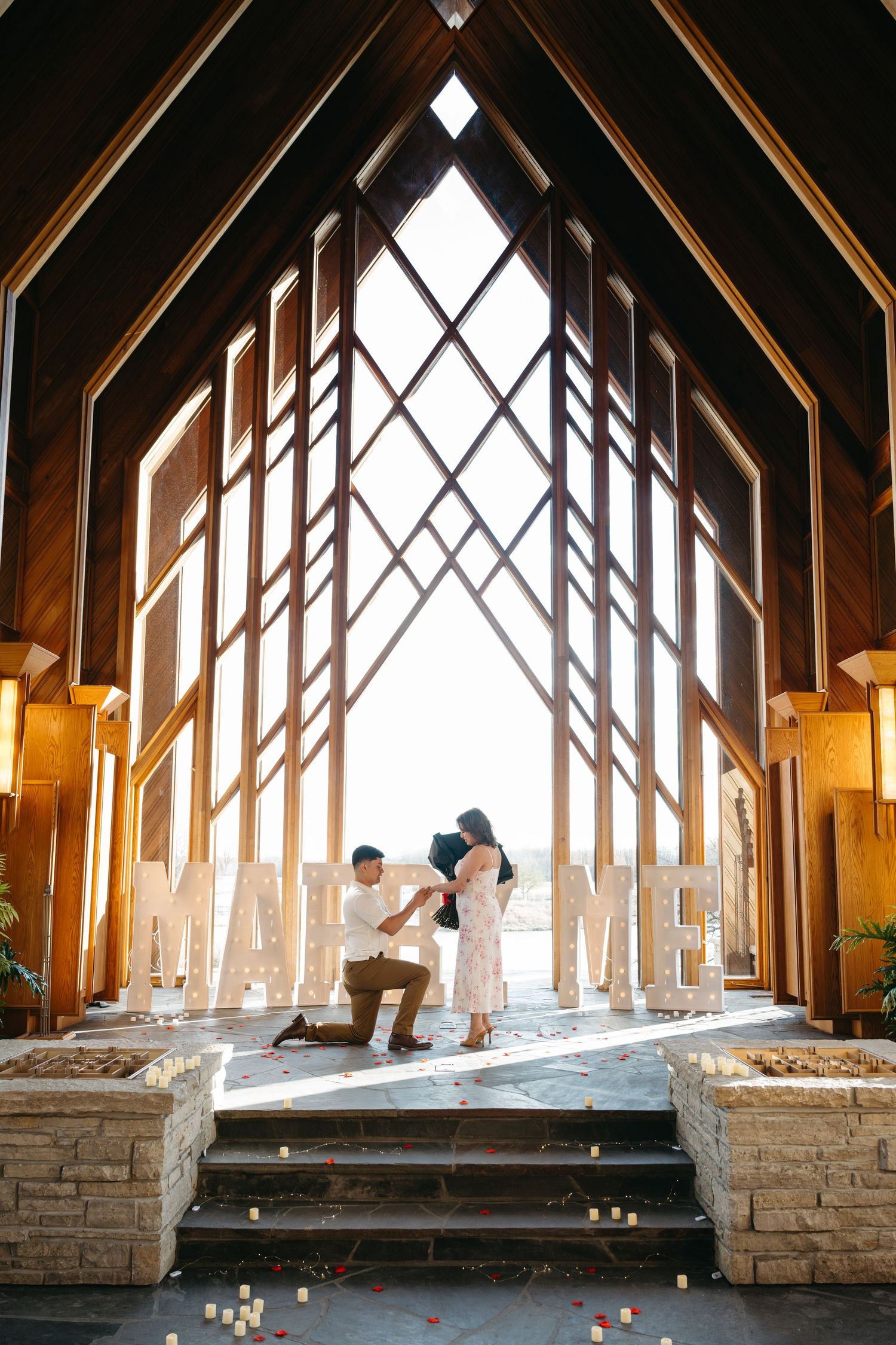 Candlelit interior of a rustic chapel with wooden beams and diamond-patterned windows.